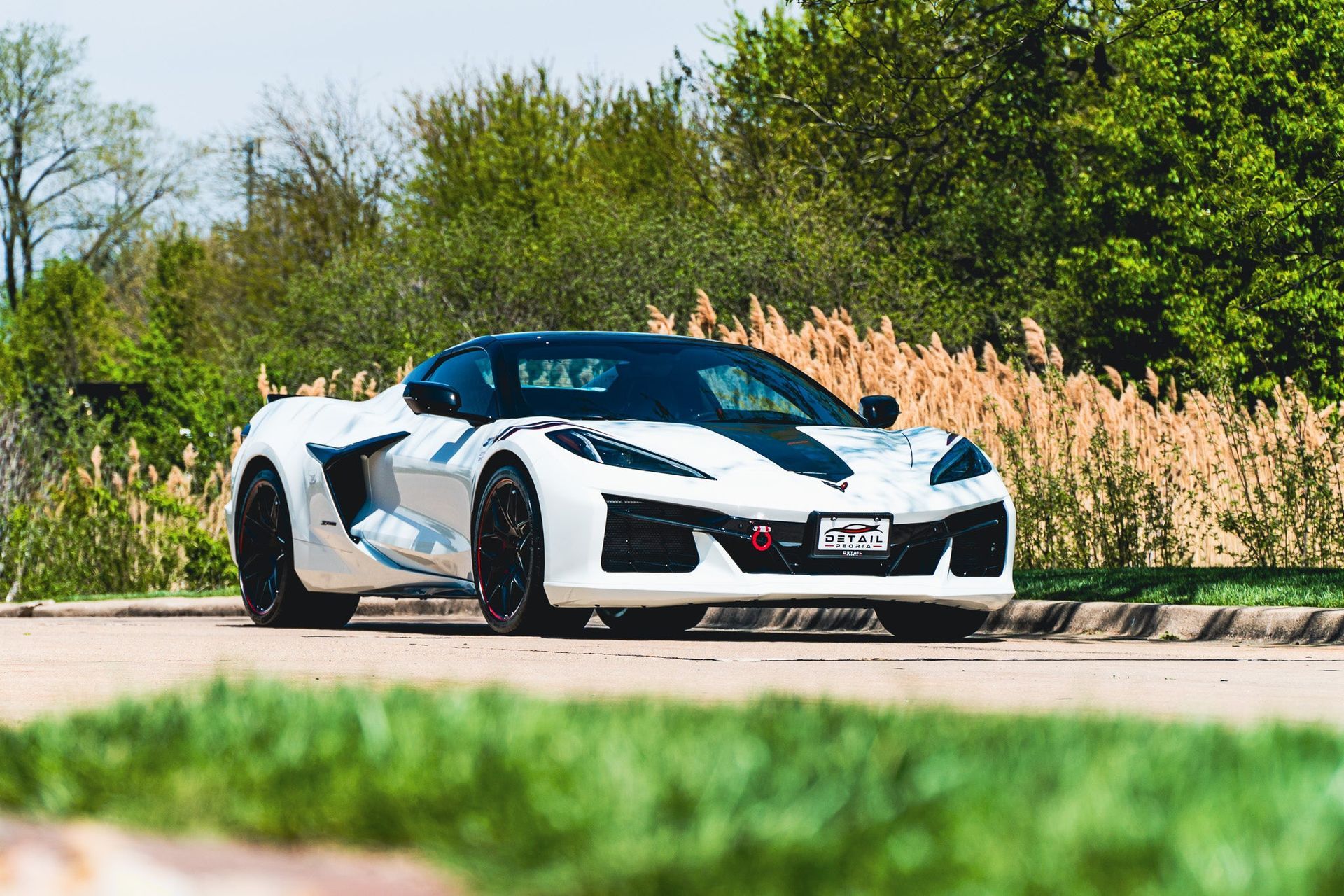 White sports car driving on a road with tall grass and trees in the background