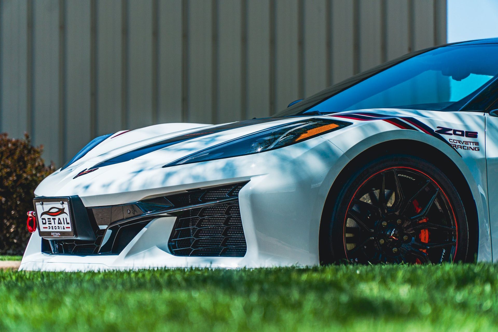 White sports car with black wheels parked on grass in front of a corrugated metal wall