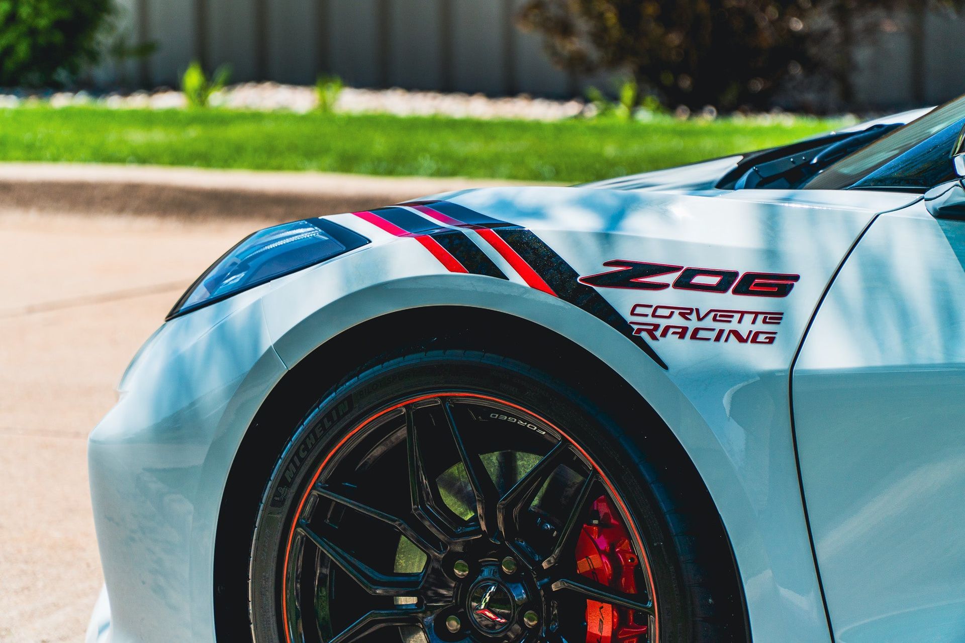 Close-up of a silver sports car’s front fender and wheel with red and black racing stripes