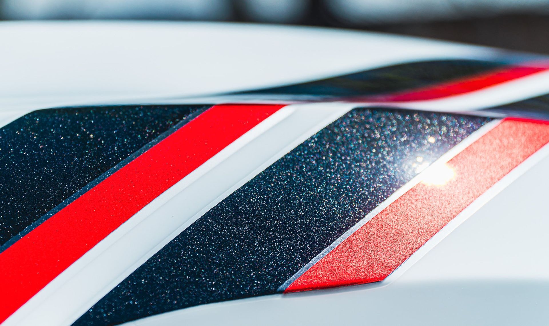 Close-up of a glossy red, white, and dark blue racing stripe design with a bright reflection on a white surface