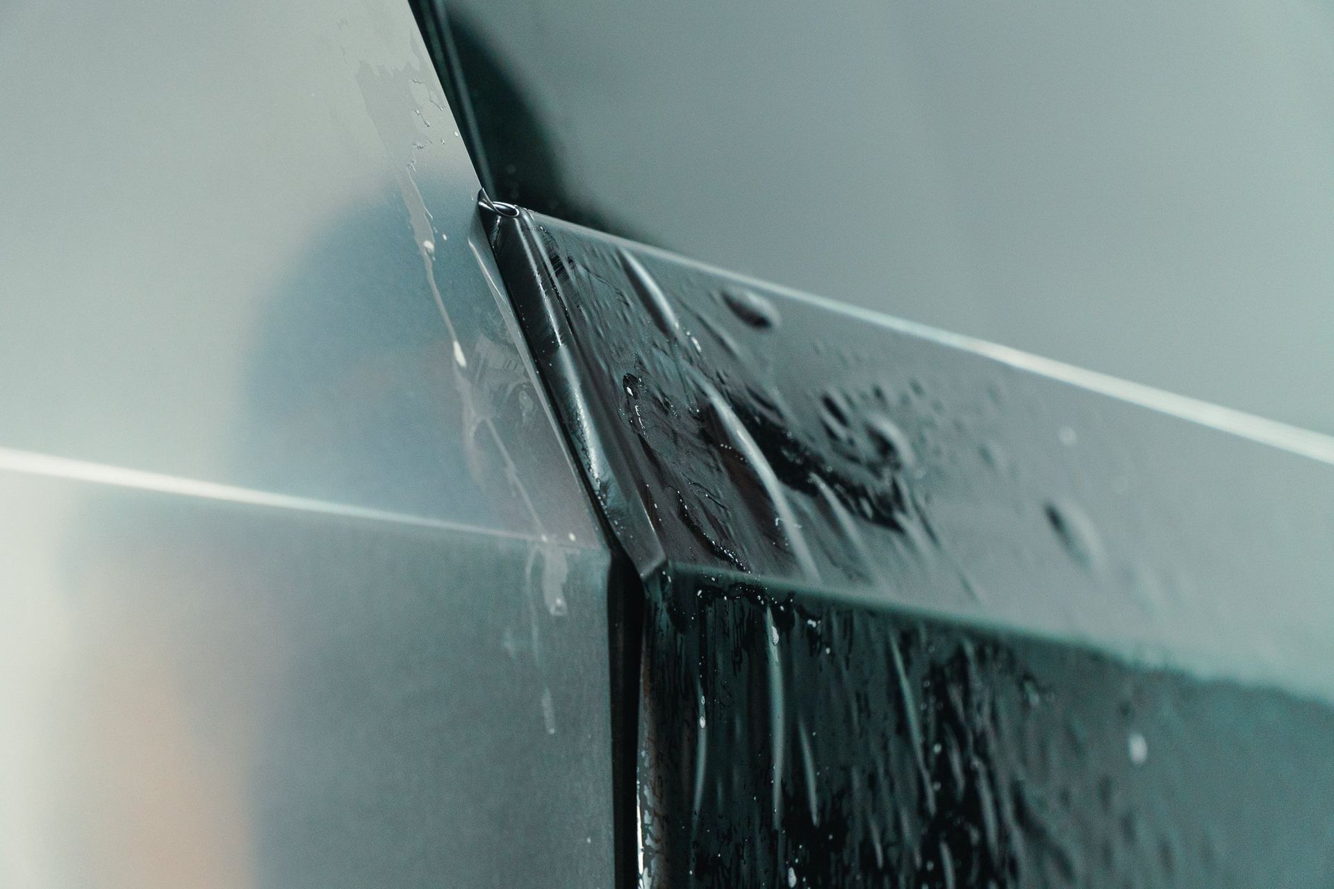 Close-up of a gray metal surface with water streaming down a seam