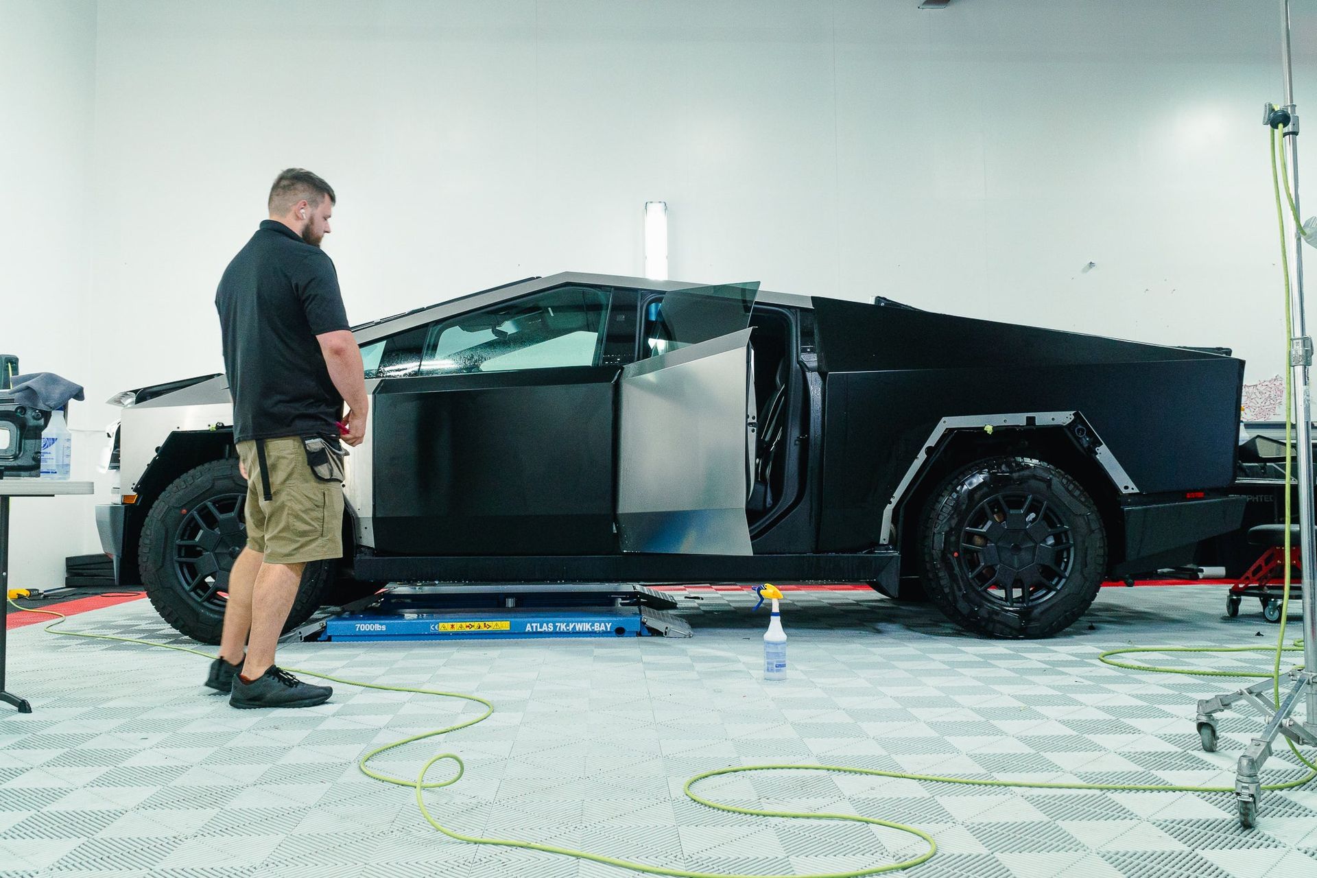 A black pickup truck in a garage with a man standing beside it and tools on the floor.