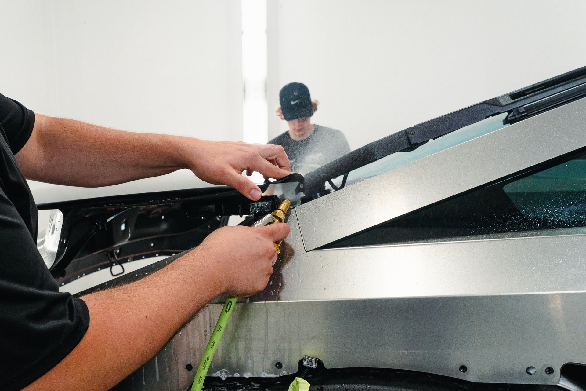 Technician working on a silver car windshield with tools in a bright garage