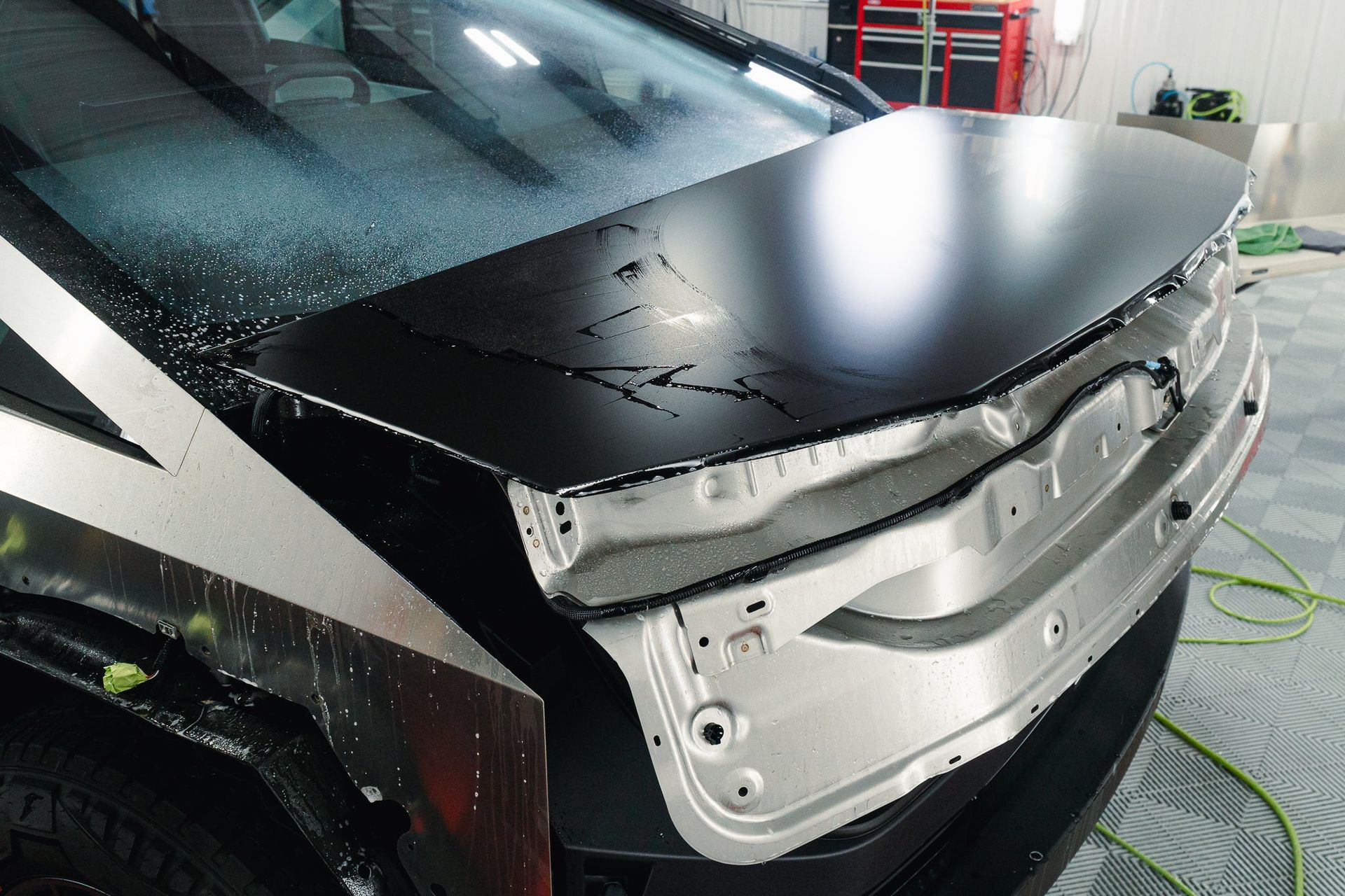 Black car with detached front bumper and exposed damaged front end in a workshop.