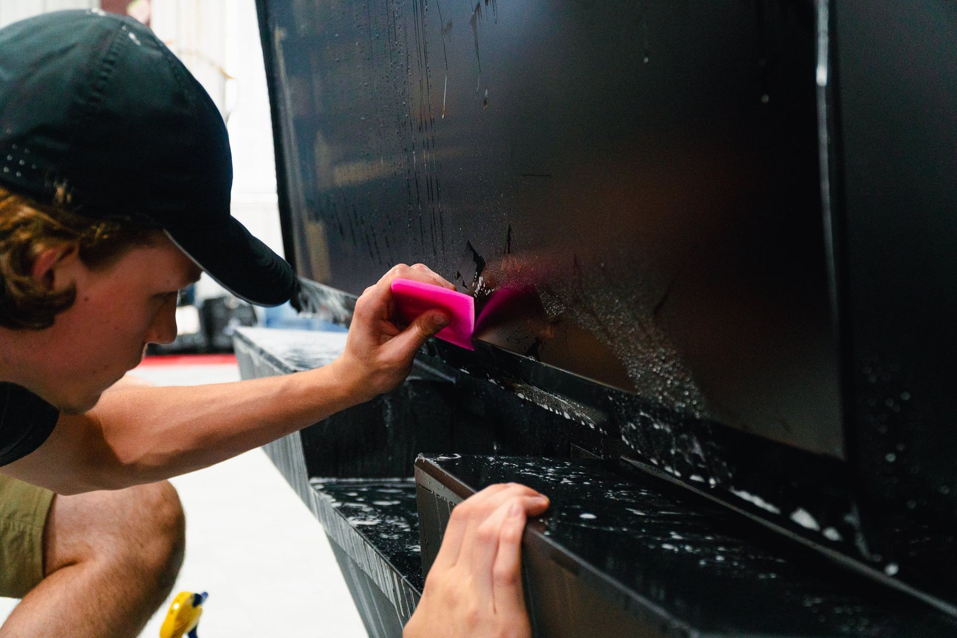 Person applying pink tape to a large black surface outdoors