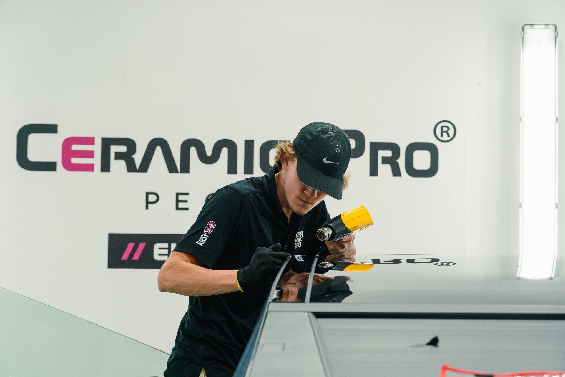 Person polishing a car at a Ceramic Pro event, wearing a black cap and shirt.