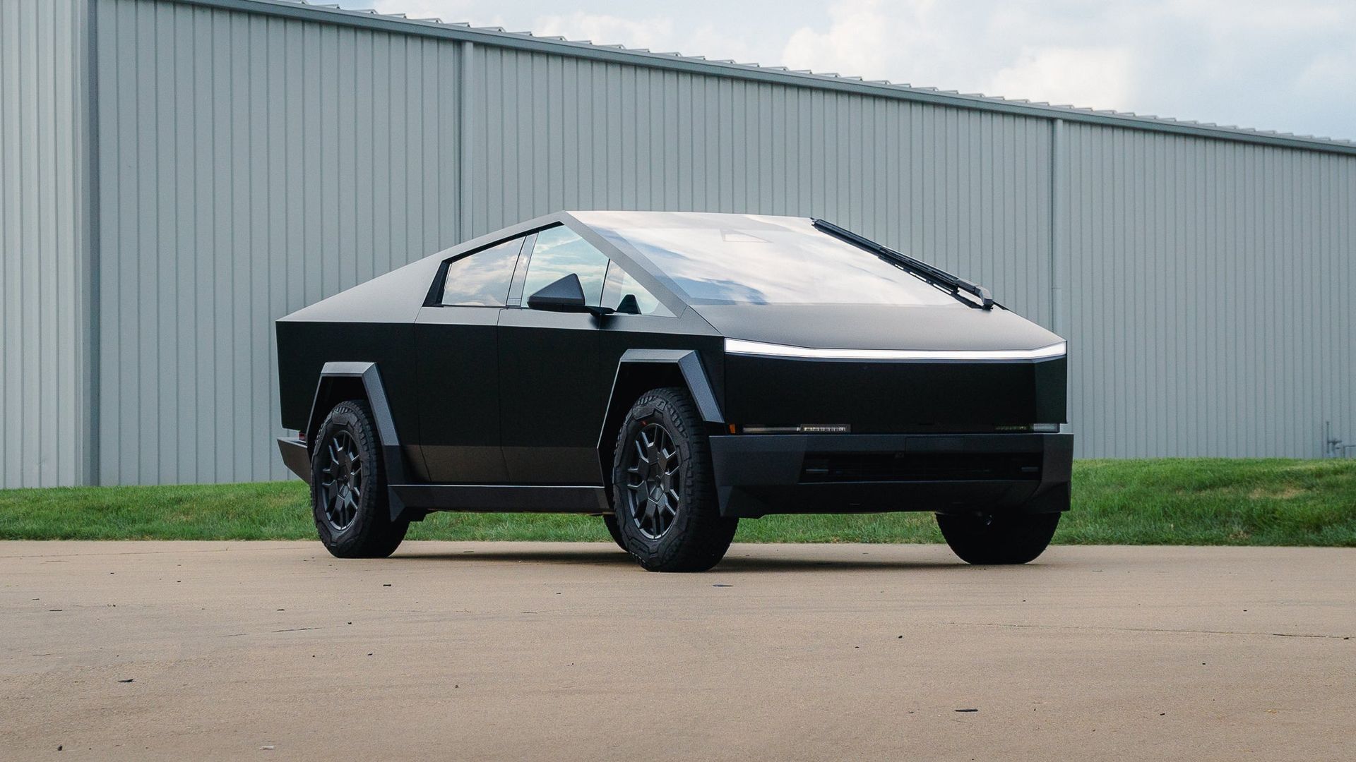 Black Tesla Cybertruck parked on pavement in front of a gray industrial building.
