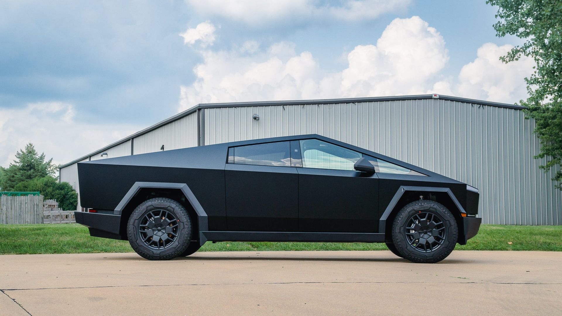 Black Tesla Cybertruck parked in front of a metal building on a sunny day