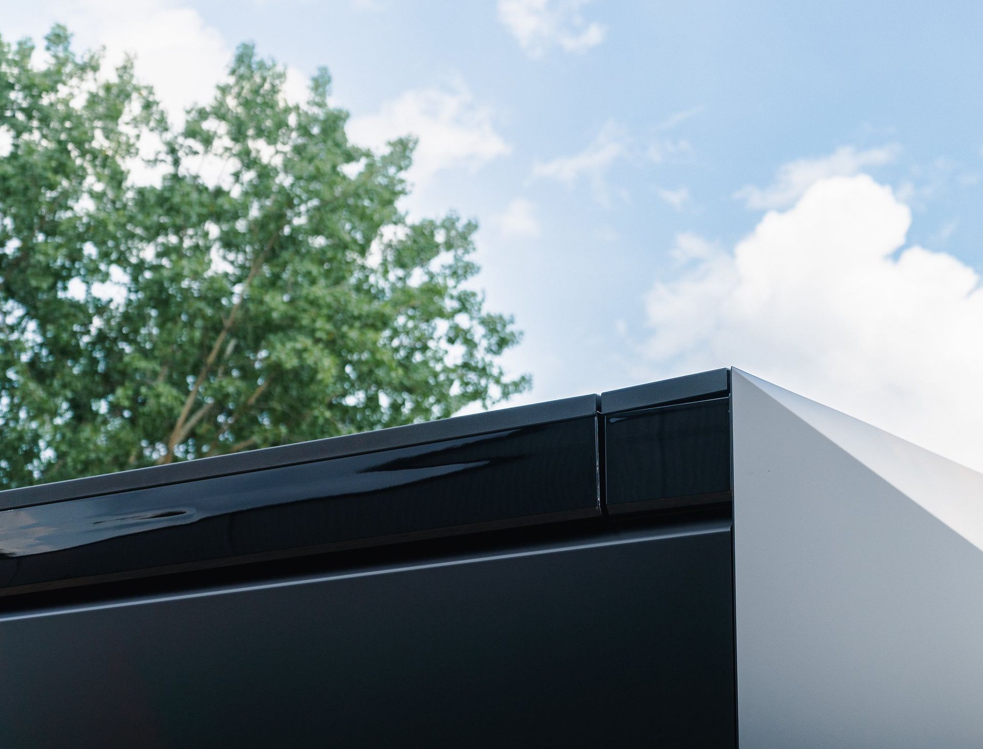 Modern building roof edge with black trim against a blue sky and green trees
