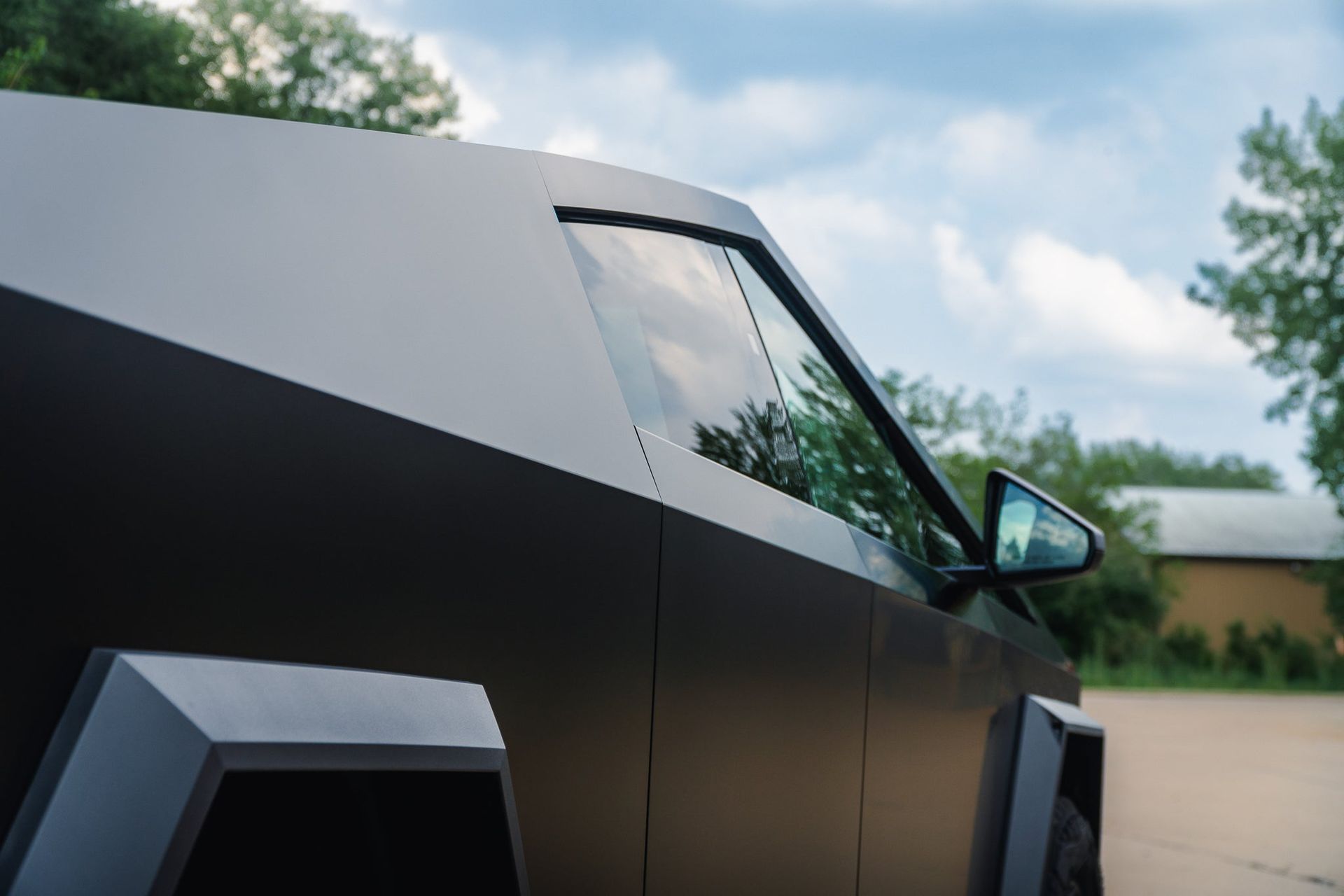 Black angular Tesla Cybertruck parked outdoors under a cloudy sky