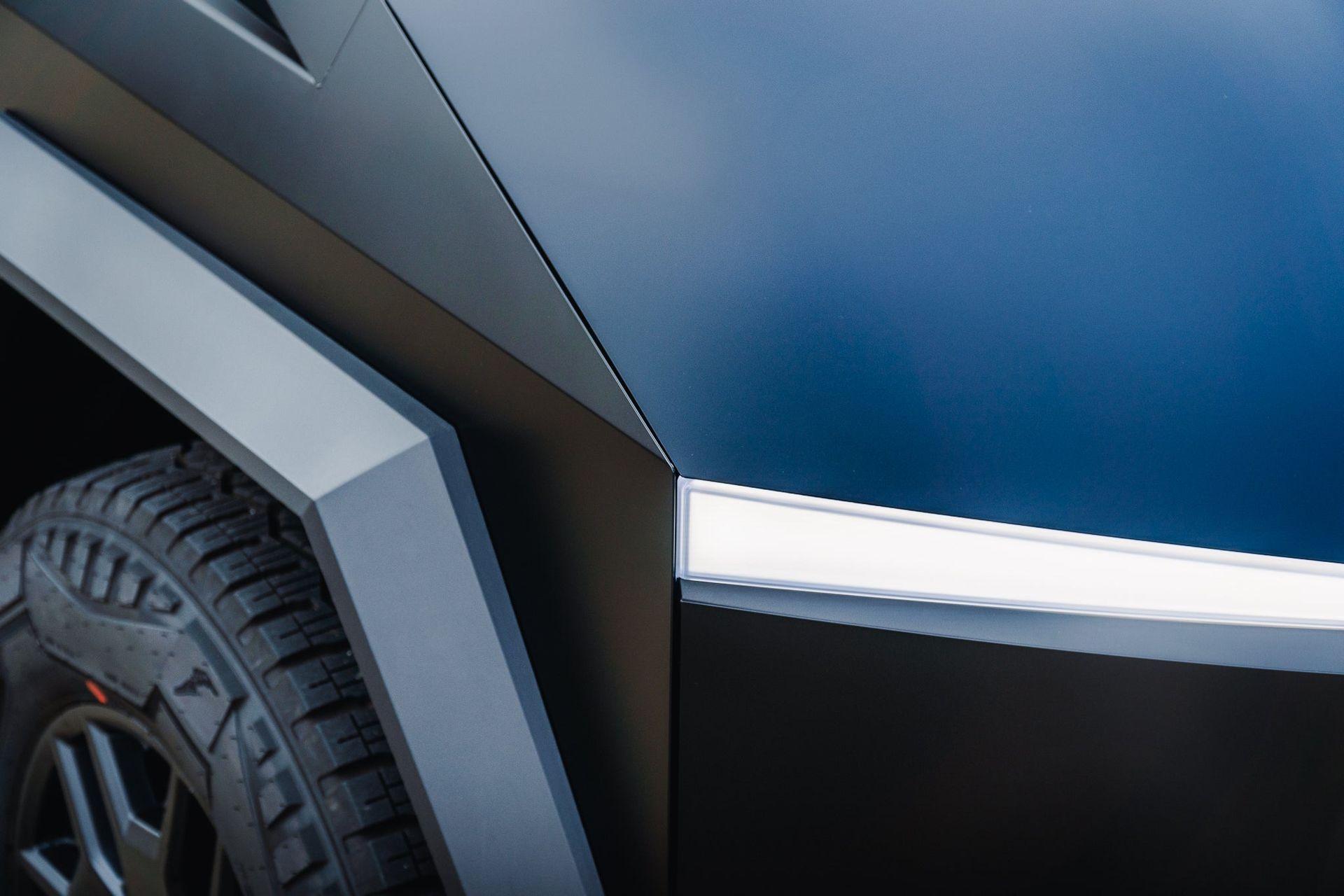 Close-up of a blue vehicle’s front fender, wheel, and silver trim against a dark background