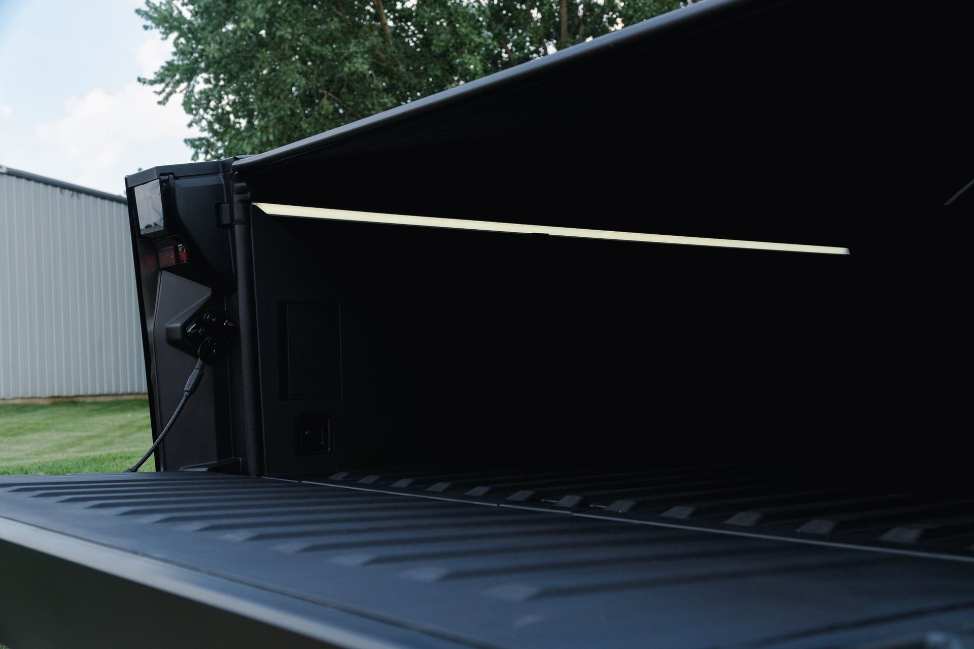 Dark empty cargo container with a partly open black door and corrugated metal floor, outdoors near a building