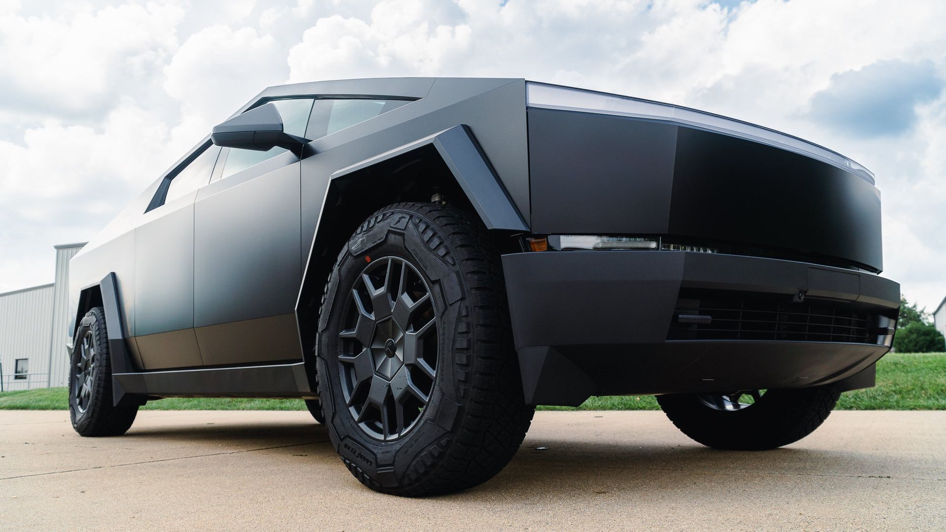 Black angular electric pickup truck parked outdoors on a road under cloudy skies