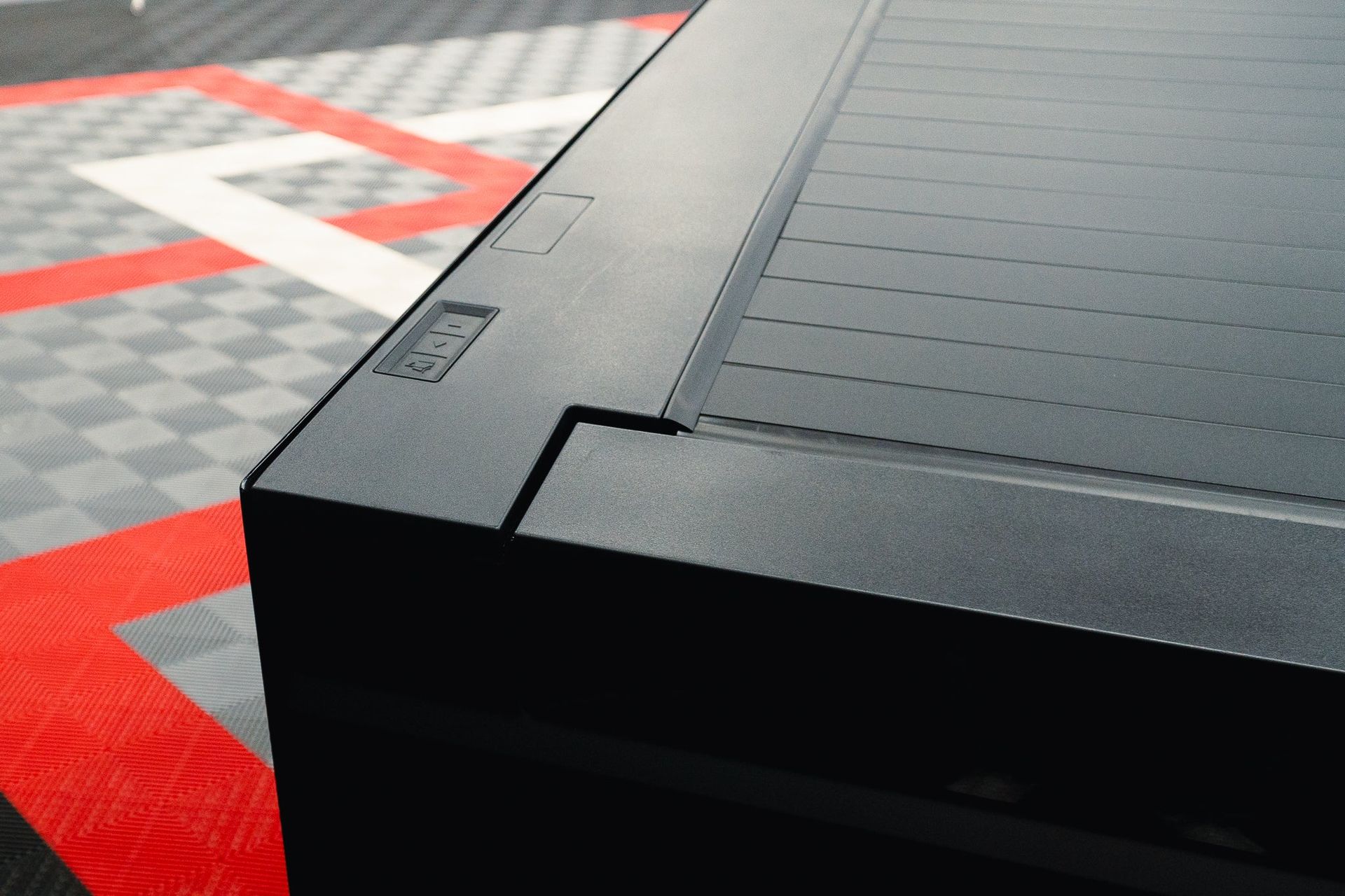 Black textured hard case corner on a red-and-gray patterned surface