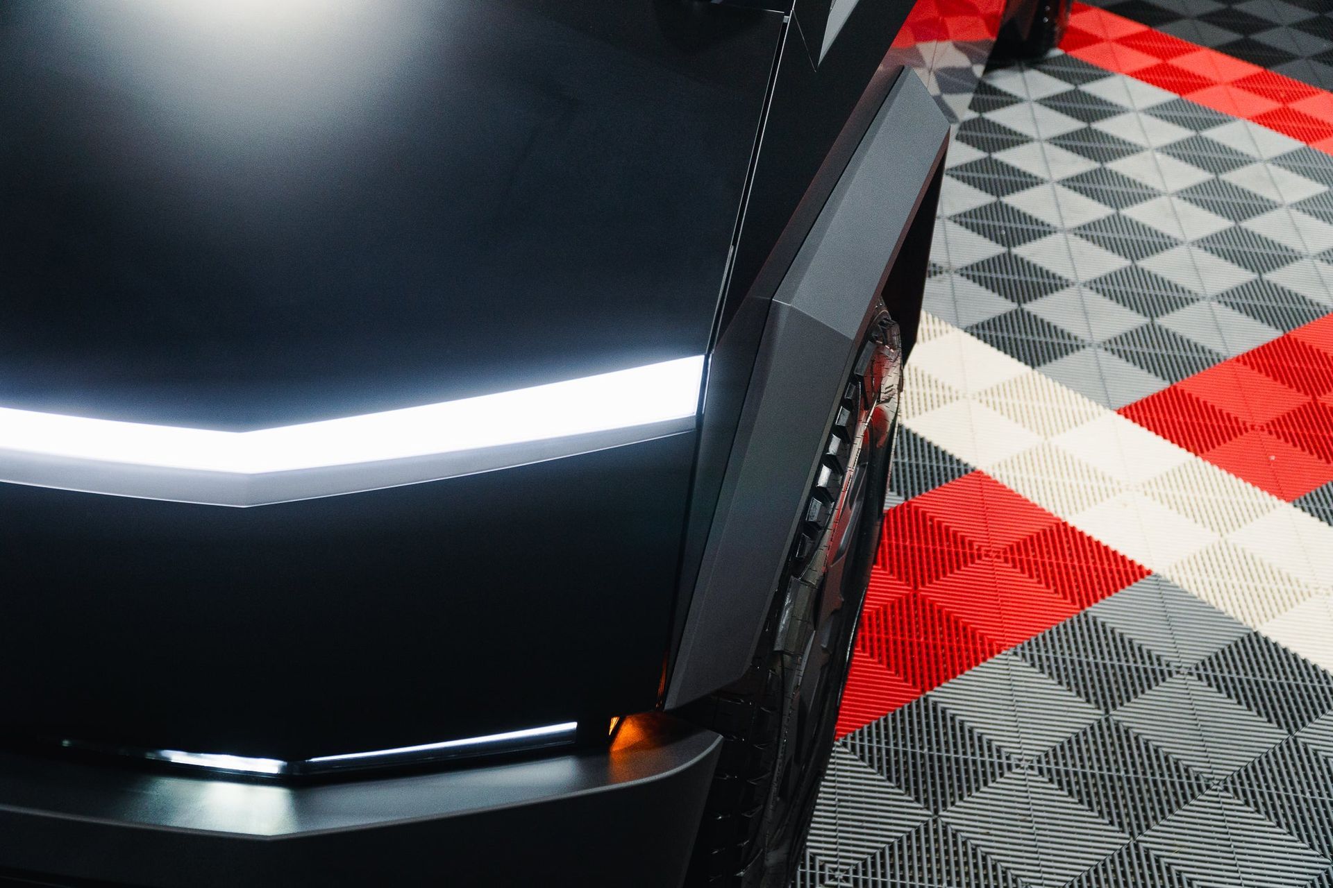 Close-up of a black car front corner with a white light strip on a checkered garage floor