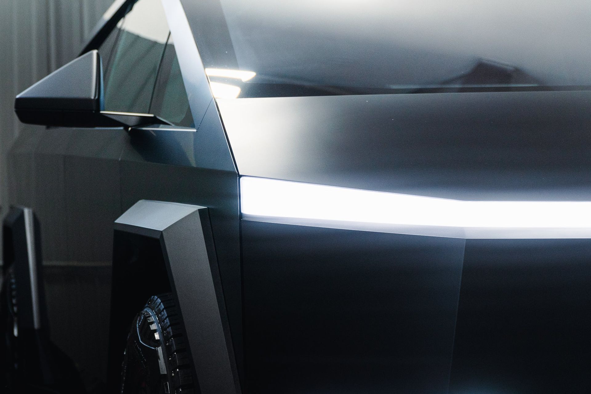 Close-up of a sleek black futuristic car with angular panels and a bright white light strip