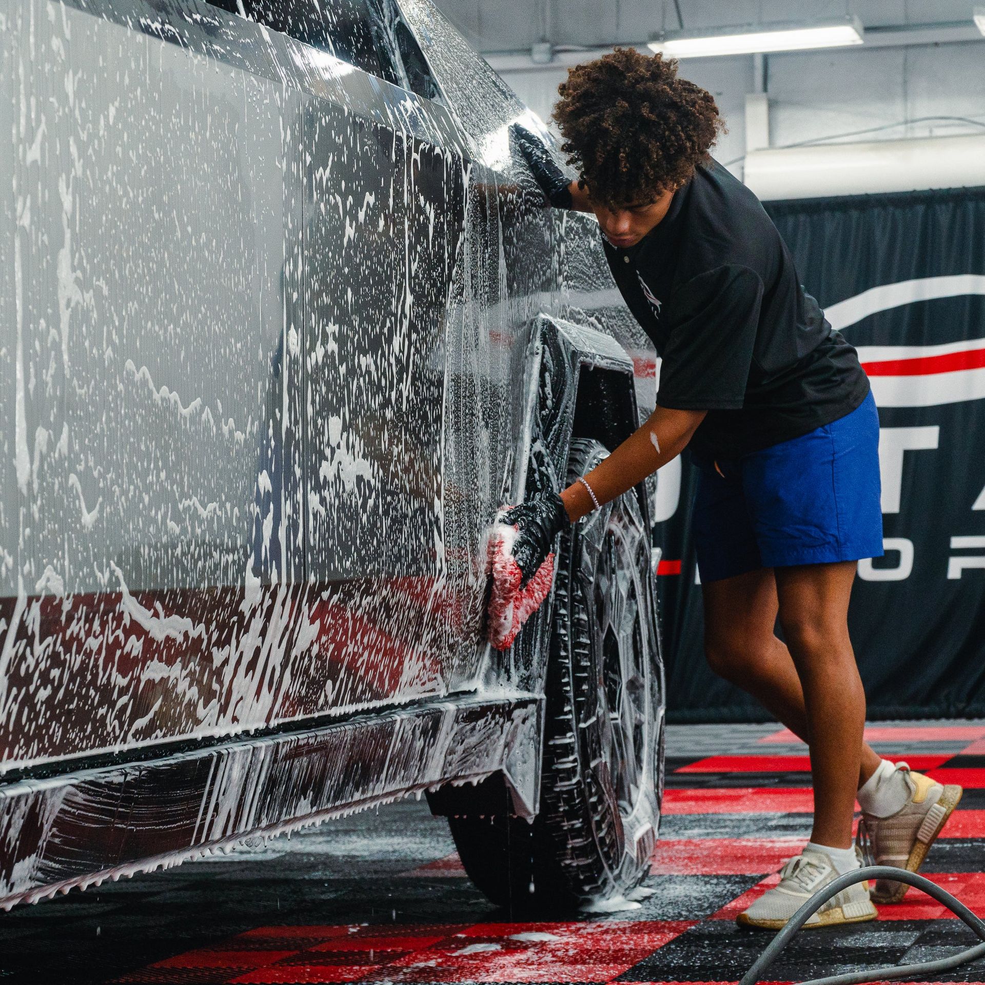 Person washing a black car with a hose in an indoor auto detail bay