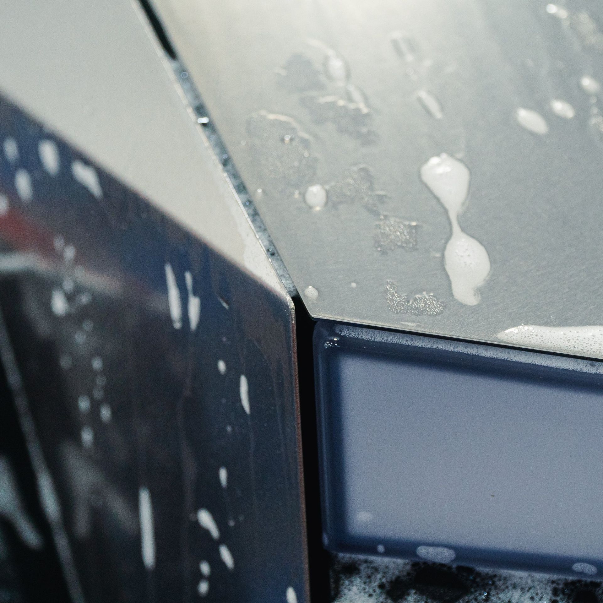 Close-up of a car corner with dark panels and white soap suds on the gray surface