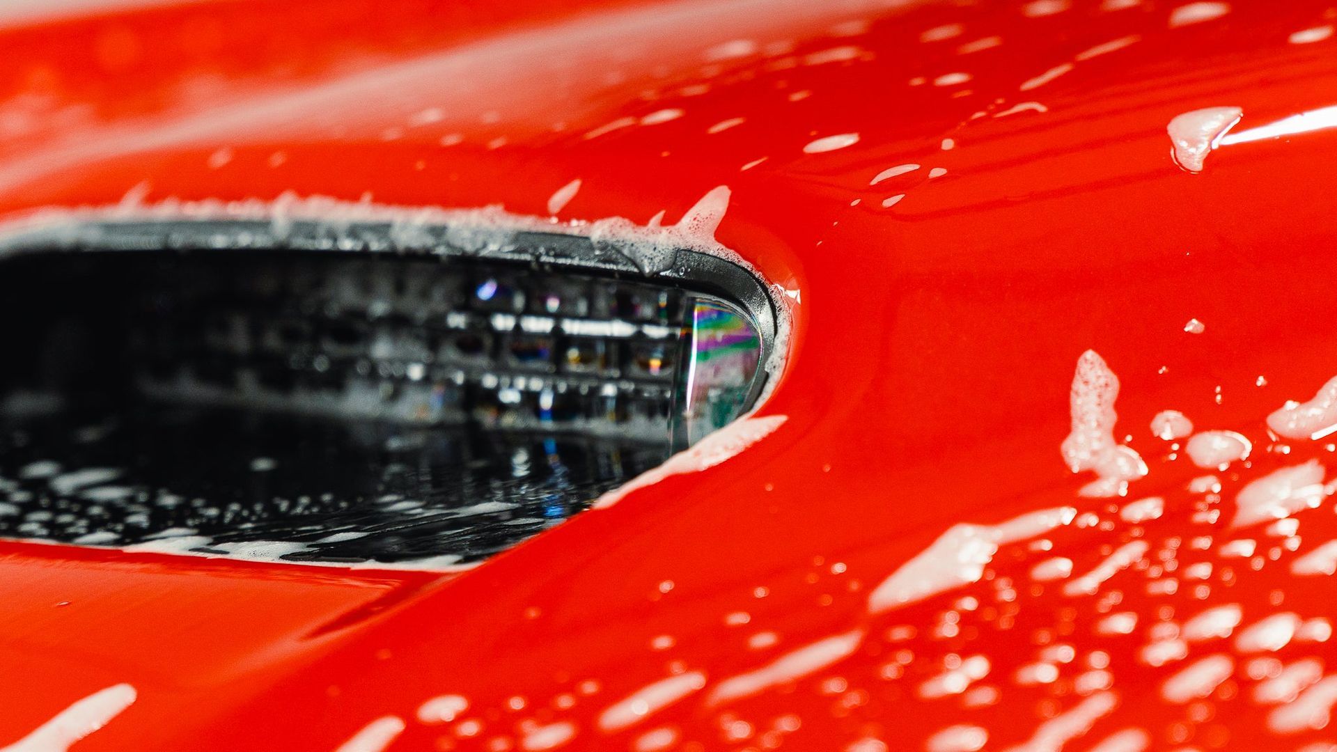 Close-up of a red car being washed, with soap suds on the body and grille