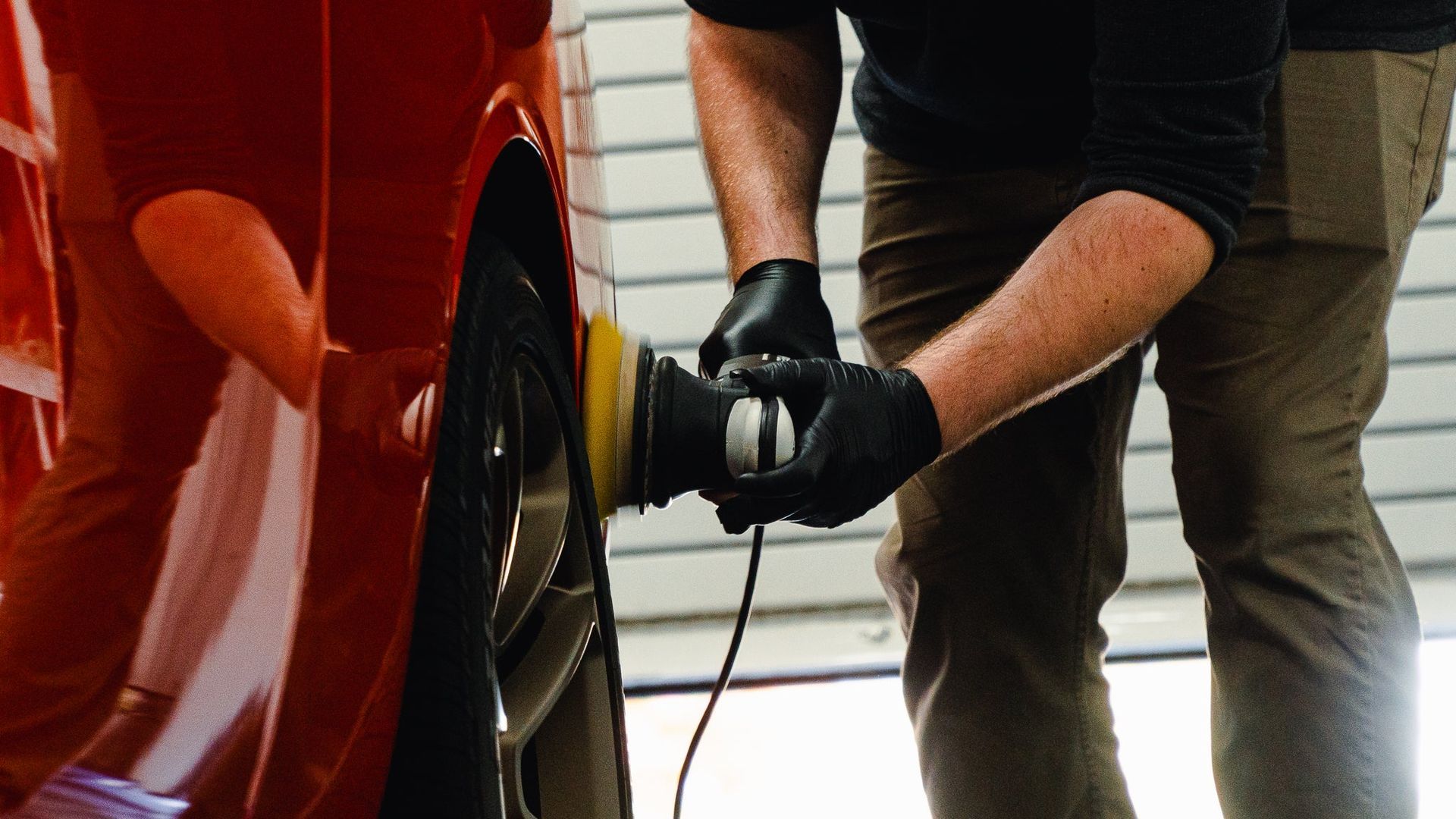 Person using a buffer to polish a red car wheel arch in a garage