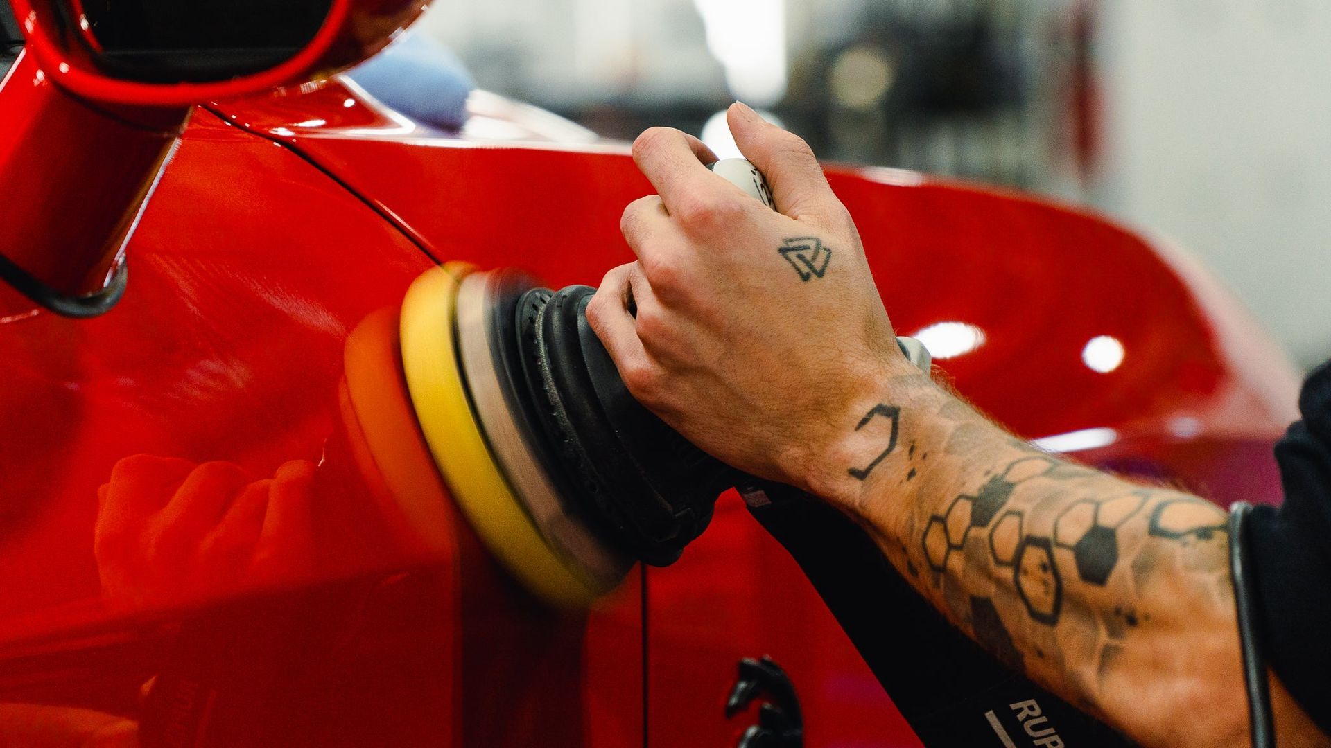 Close-up of a tattooed hand gripping a red motorcycle with a black and yellow glove cuff