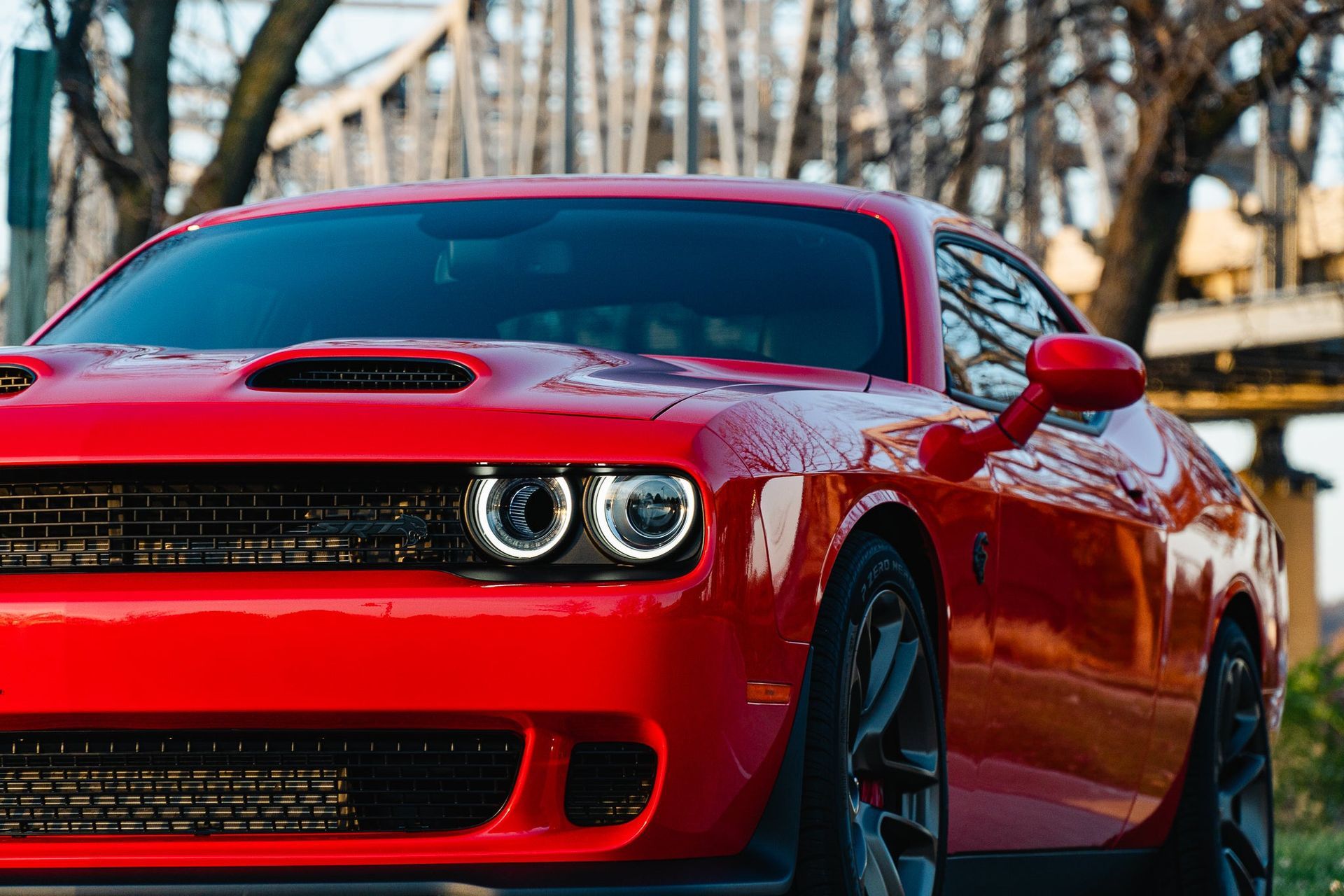 Red sports car parked outdoors with headlights on, trees in the background