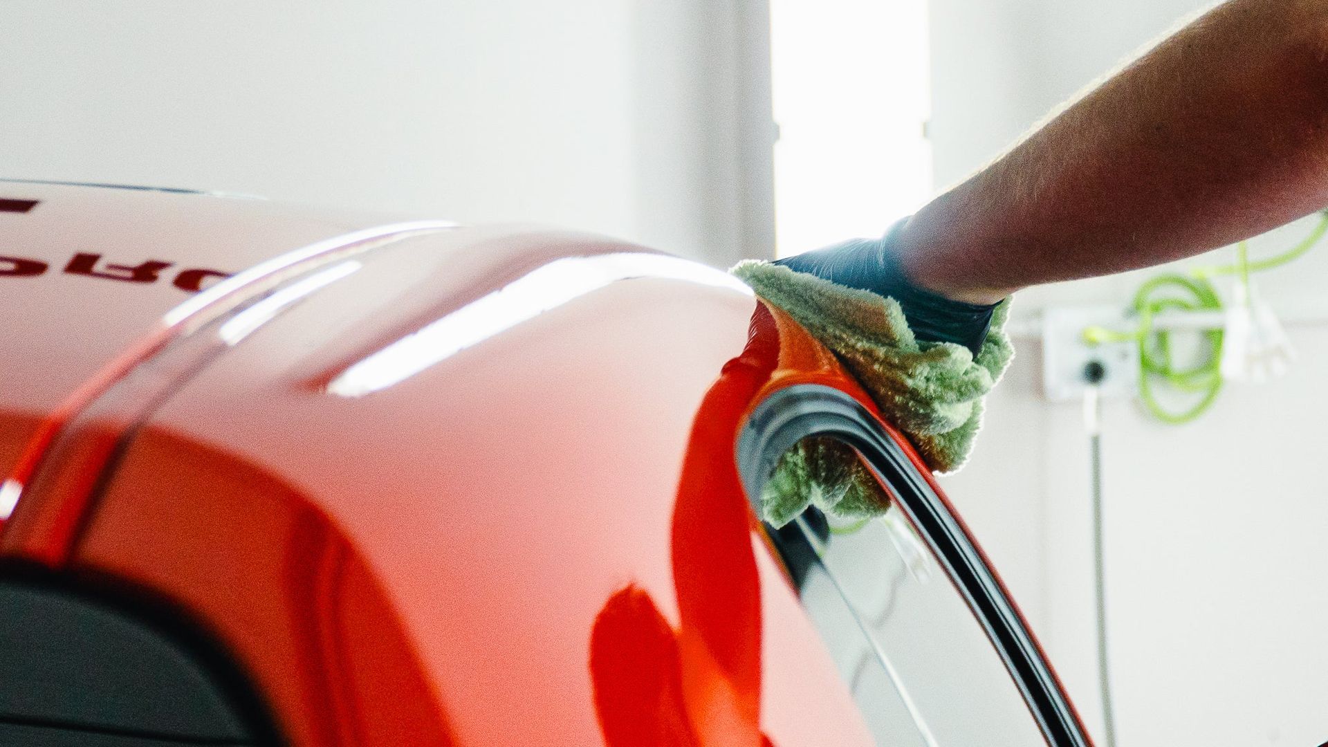 Hand scrubbing a glossy red car panel with a green sponge and water spray