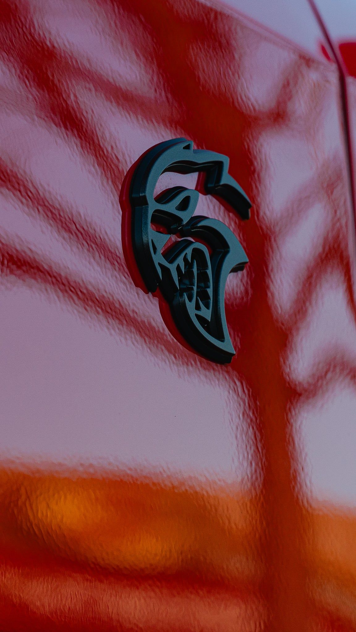 Black-and-white Spartan logo on a red vehicle, with an orange reflection at the bottom.