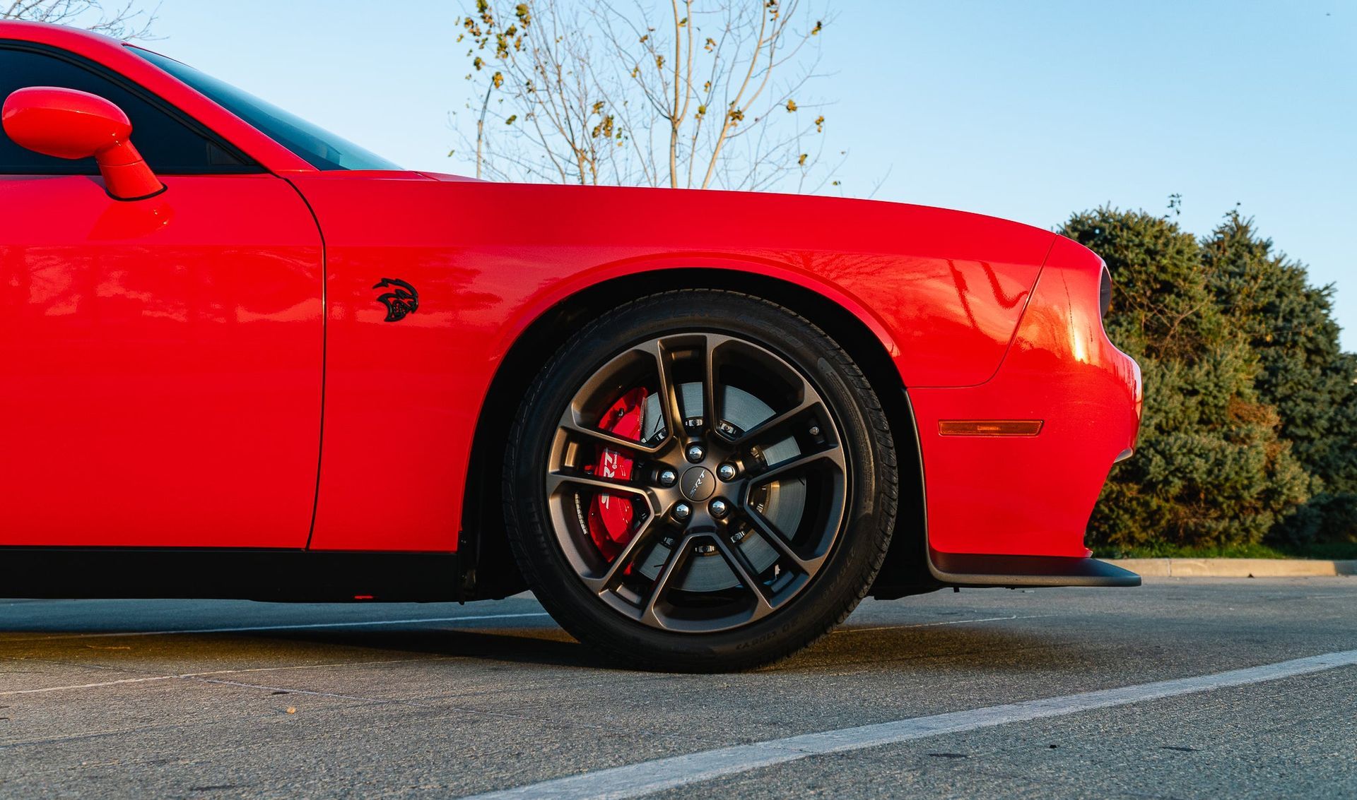Red sports car parked outdoors at sunset, showing the front wheel and side panel.