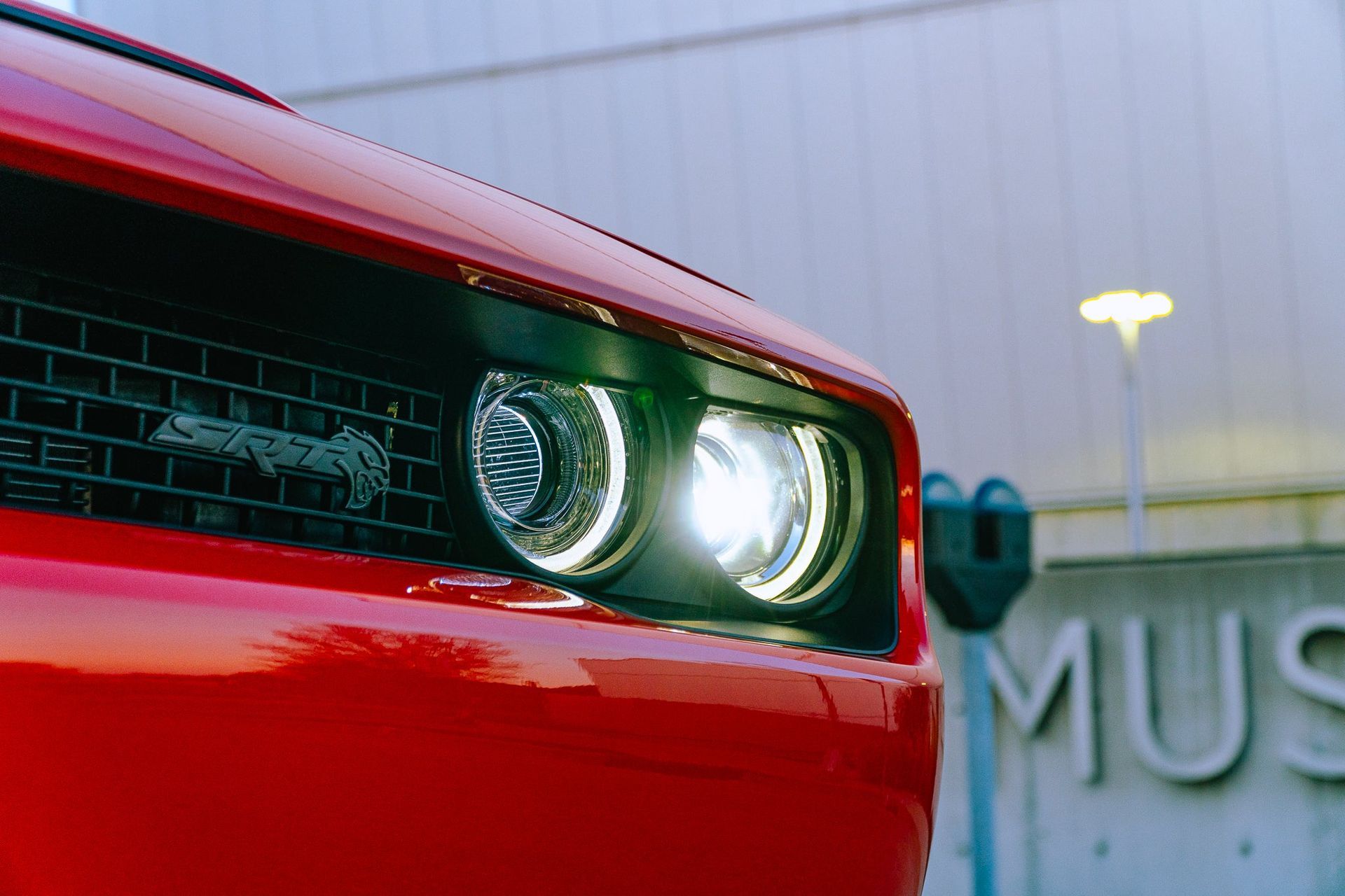 Red car front with glowing headlight beside a building sign reading “MUS”