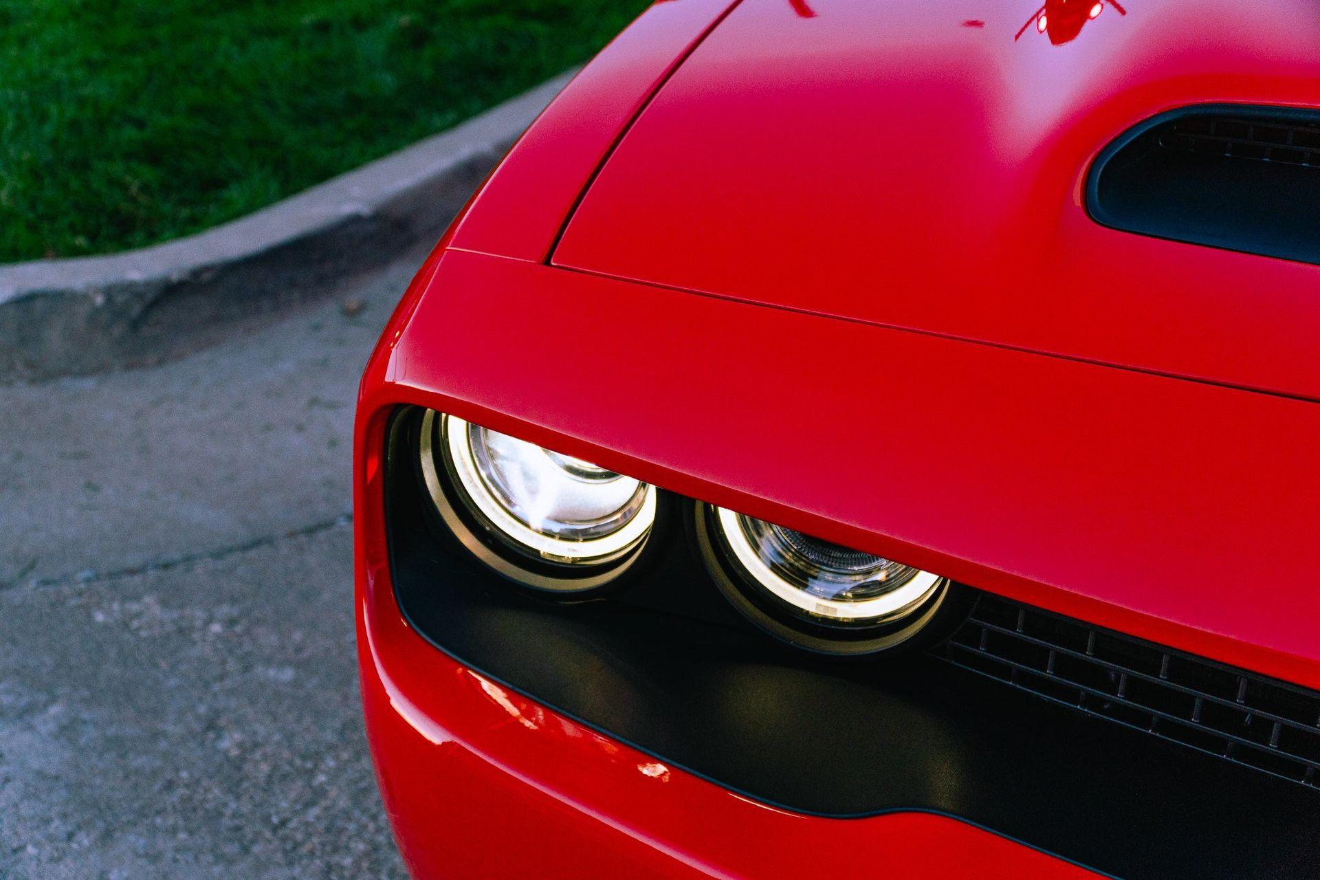 Close-up of a red sports car’s front end with twin headlights on a road.