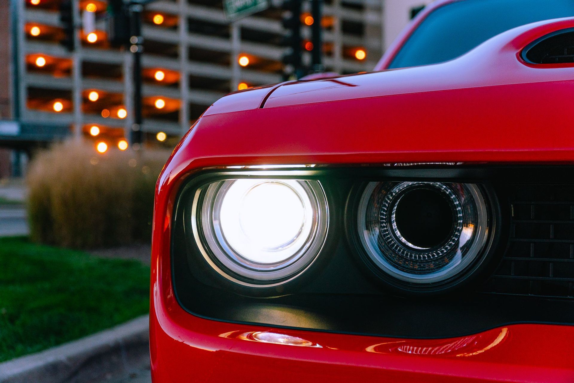 Close-up of a red sports car front headlight glowing at dusk, with city lights in the background
