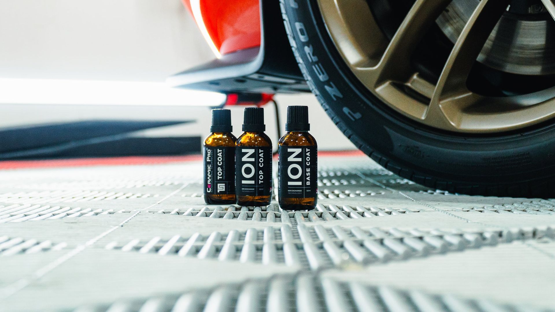 Two small black-and-orange bottles beside a car tire on a white textured surface