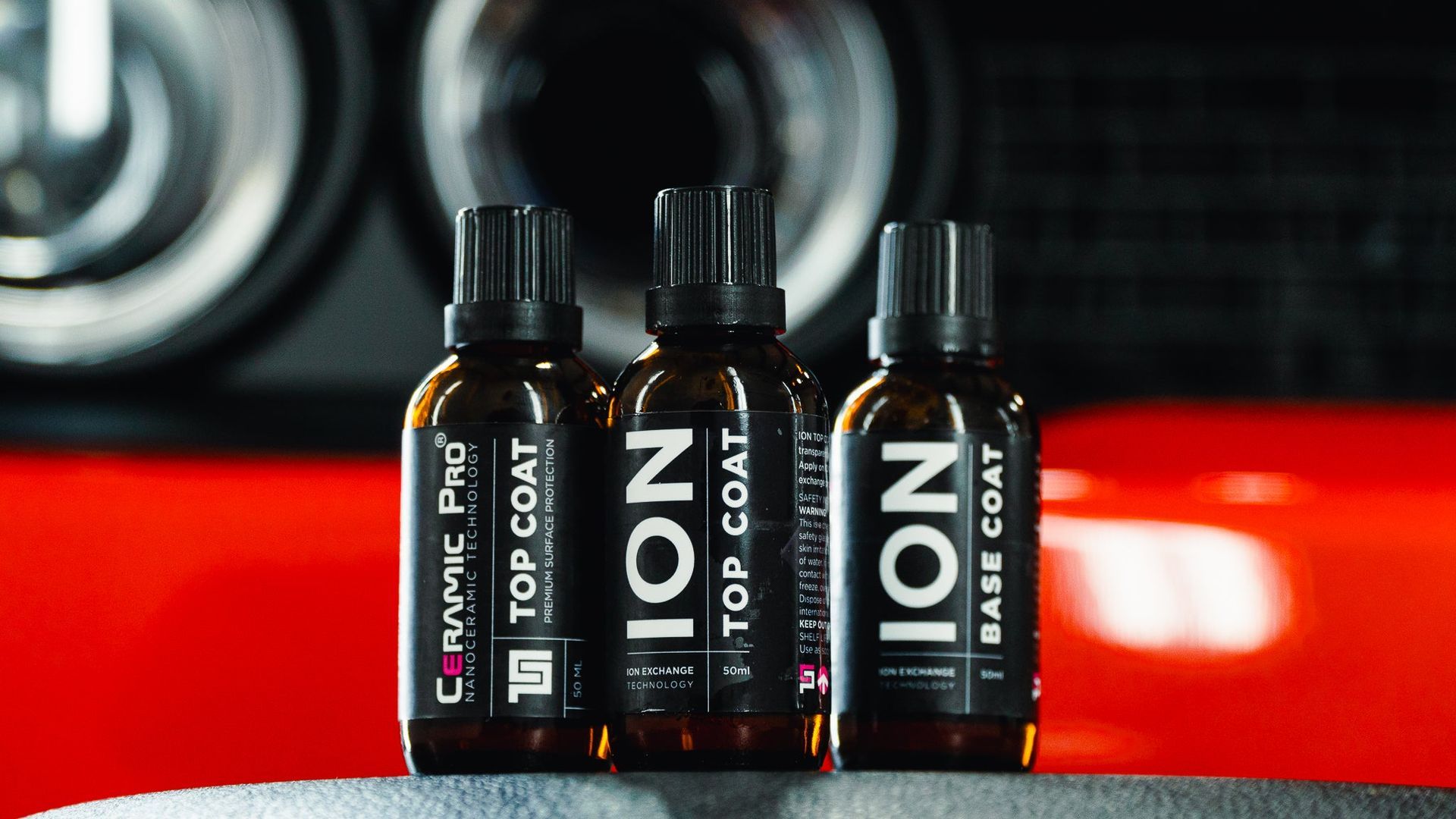 Three black ION topical bottles lined up on a red surface with a blurred car wheel in the background