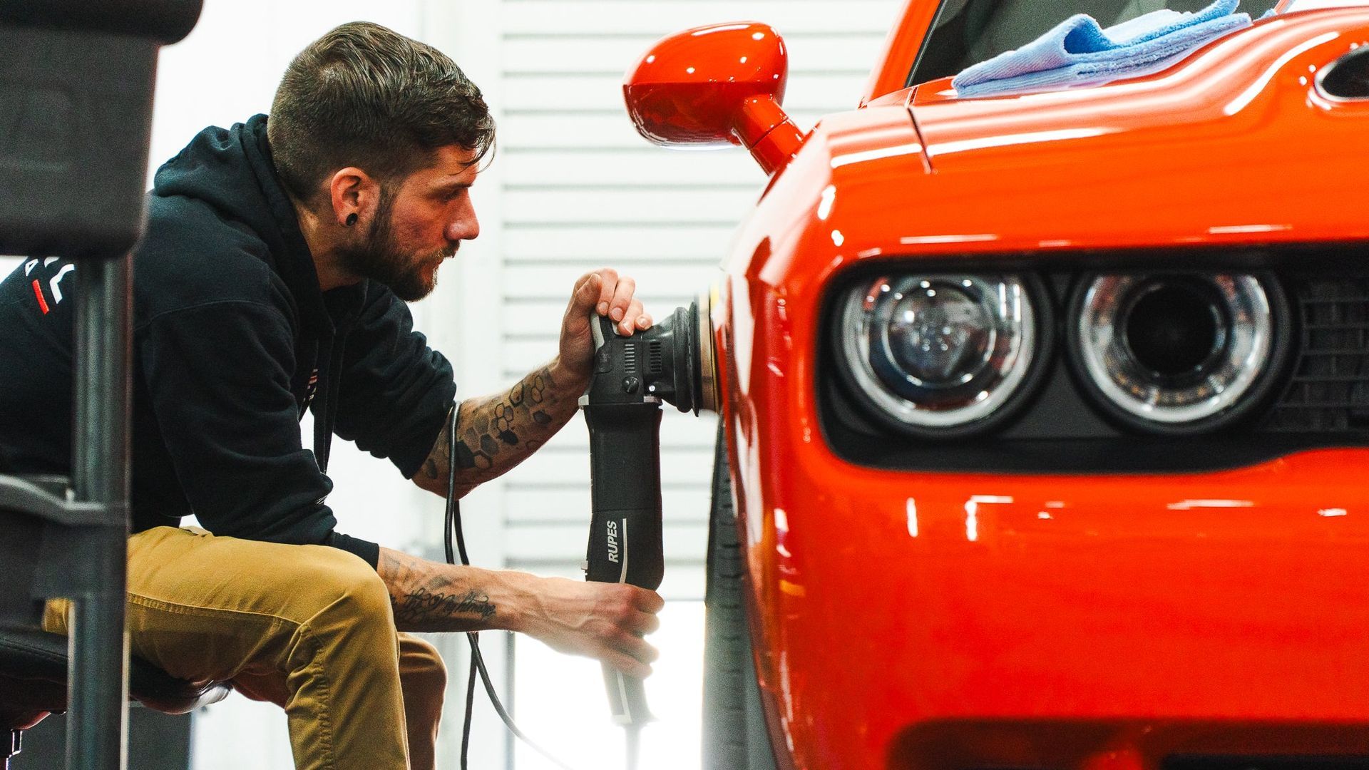 Mechanic polishing the front of a bright orange sports car in a garage