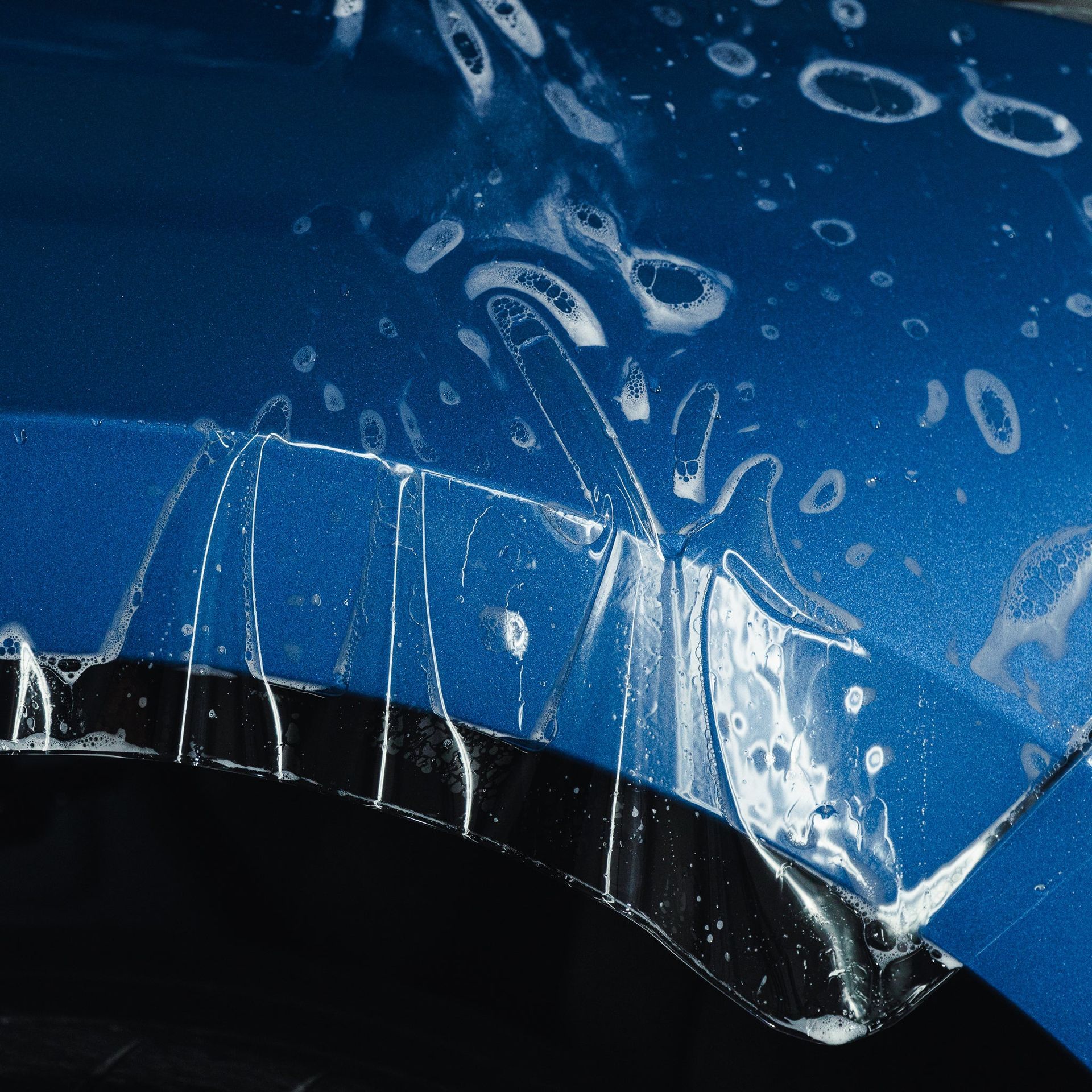 Close-up of a blue and black car hood with shattered glass and water droplets