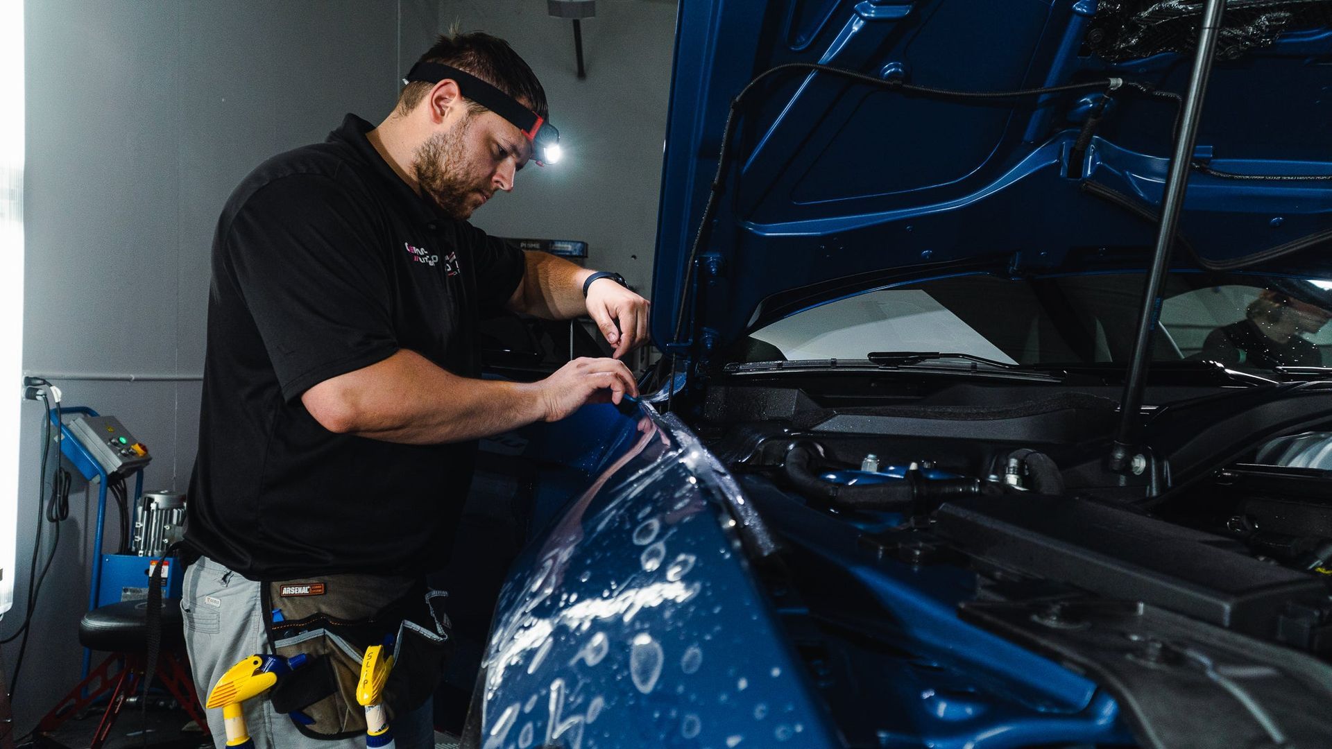 Mechanic working under the hood of a blue car in a garage