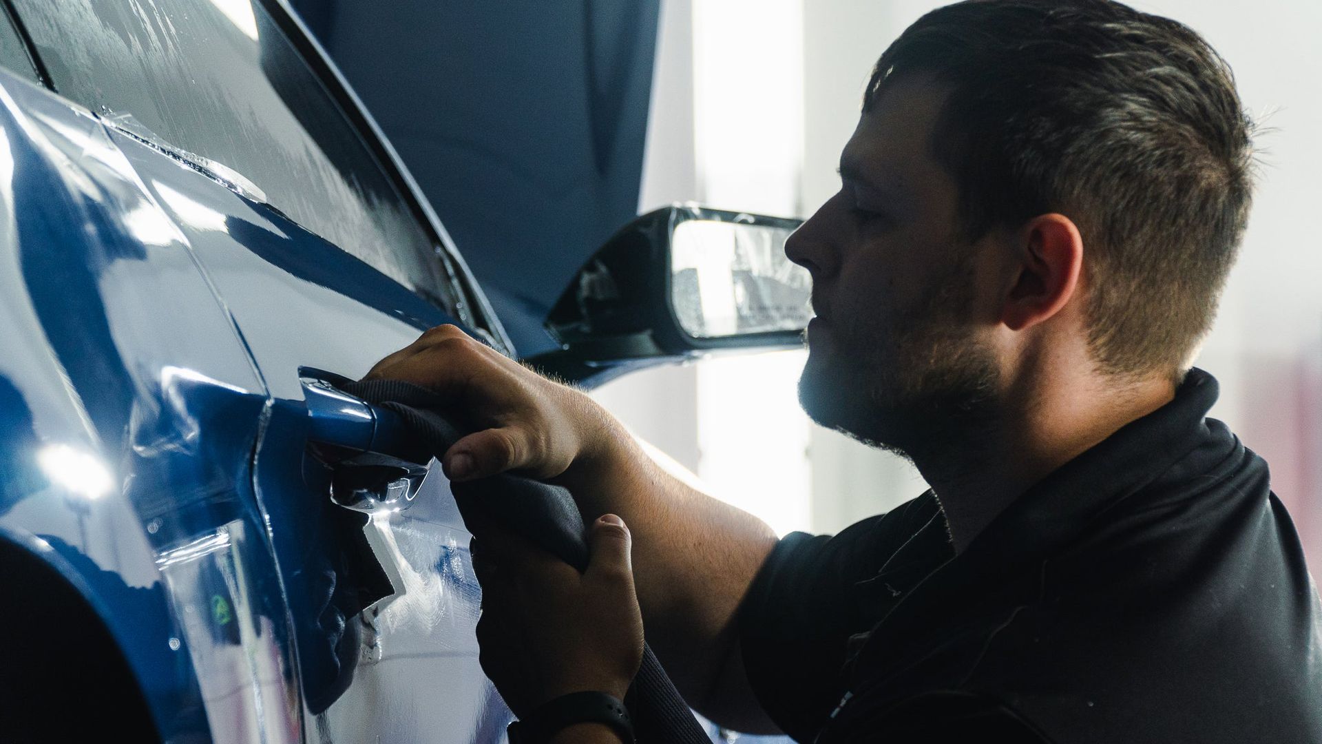Man polishing a blue car with a cloth in a workshop
