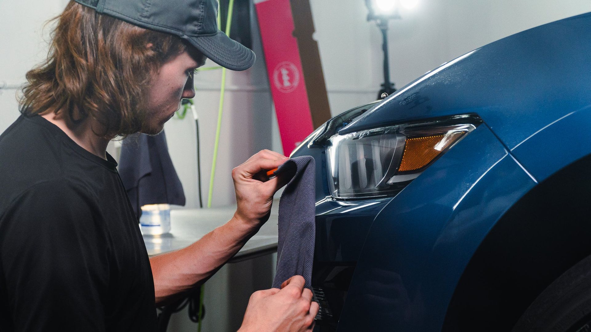Mechanic polishing the front of a blue car in a garage