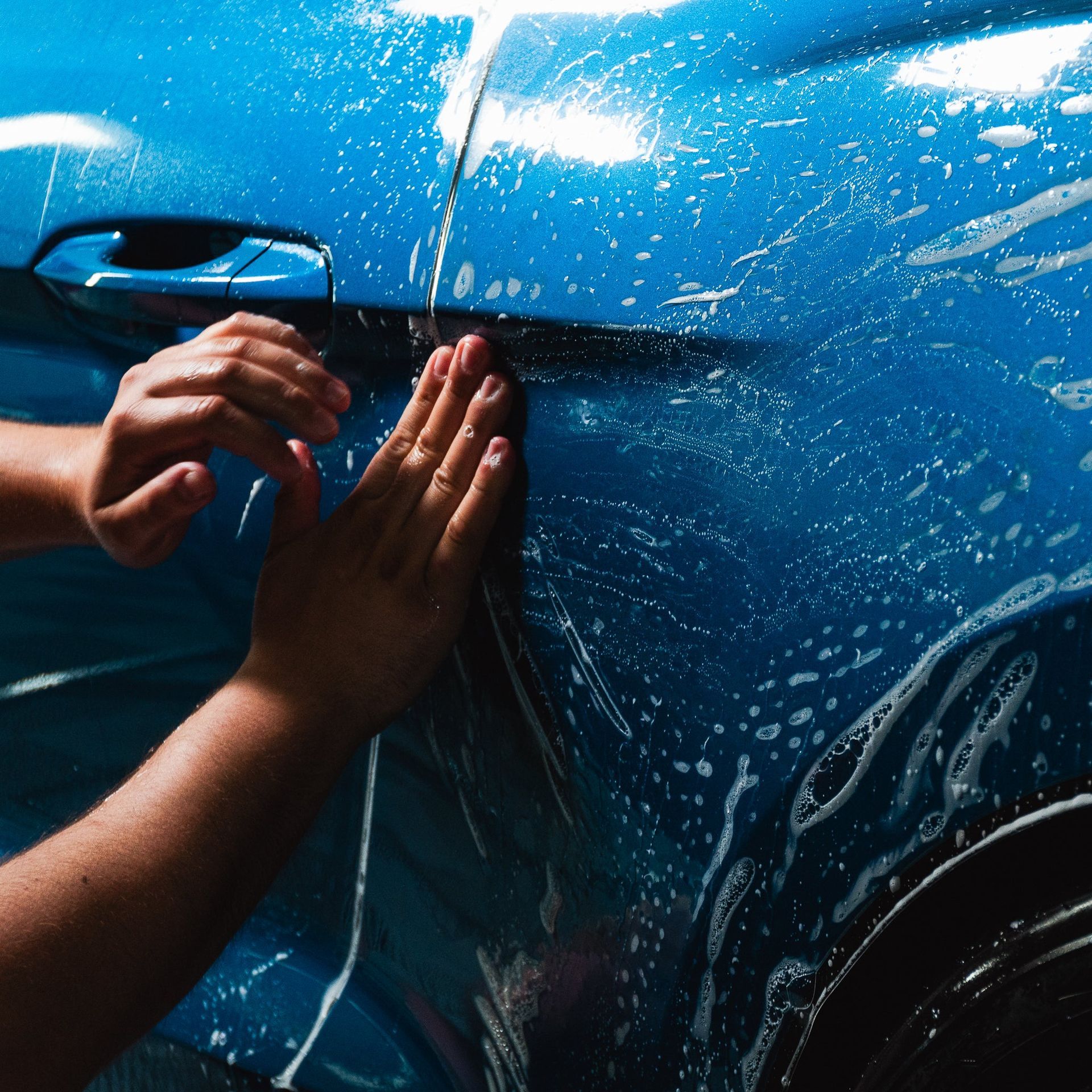 Hands washing mud off a blue car door outdoors