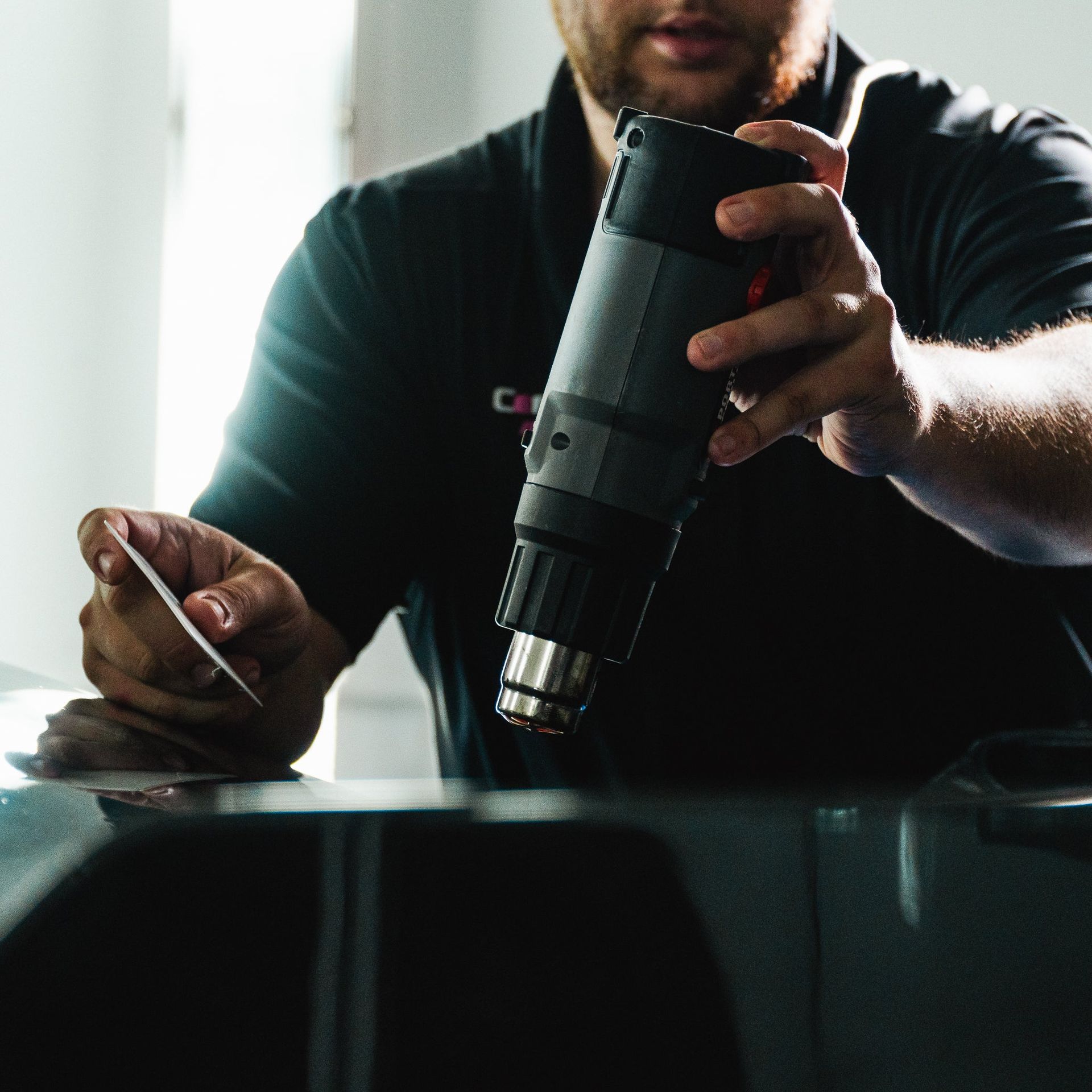 Person using a heat gun on a dark surface while holding a small tool in a workshop-like setting