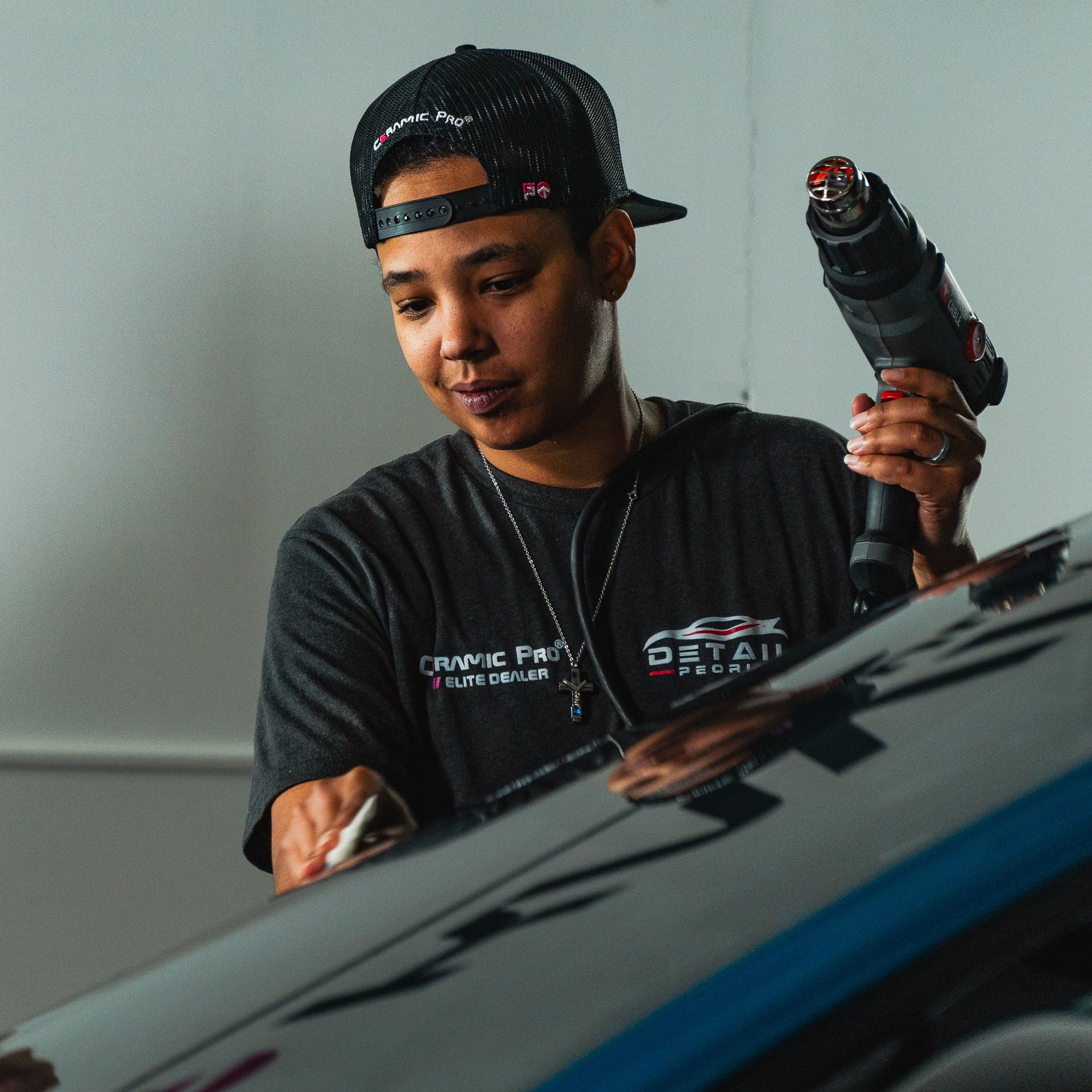 Mechanic in a black cap inspecting a car windshield with a power tool