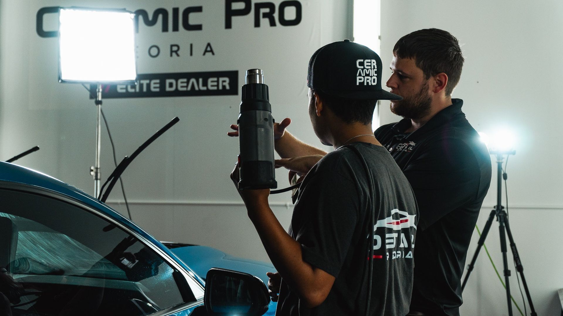 Two technicians filming a car in a studio with bright lights and a camera rig
