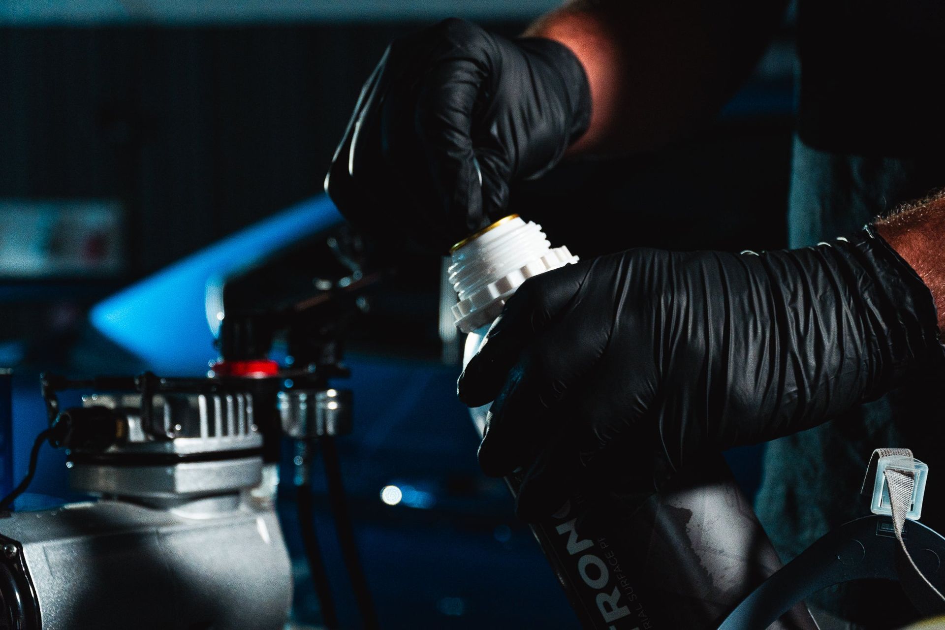 Black-gloved hands working on a car engine in a dim garage, with tools and blue lighting in the background