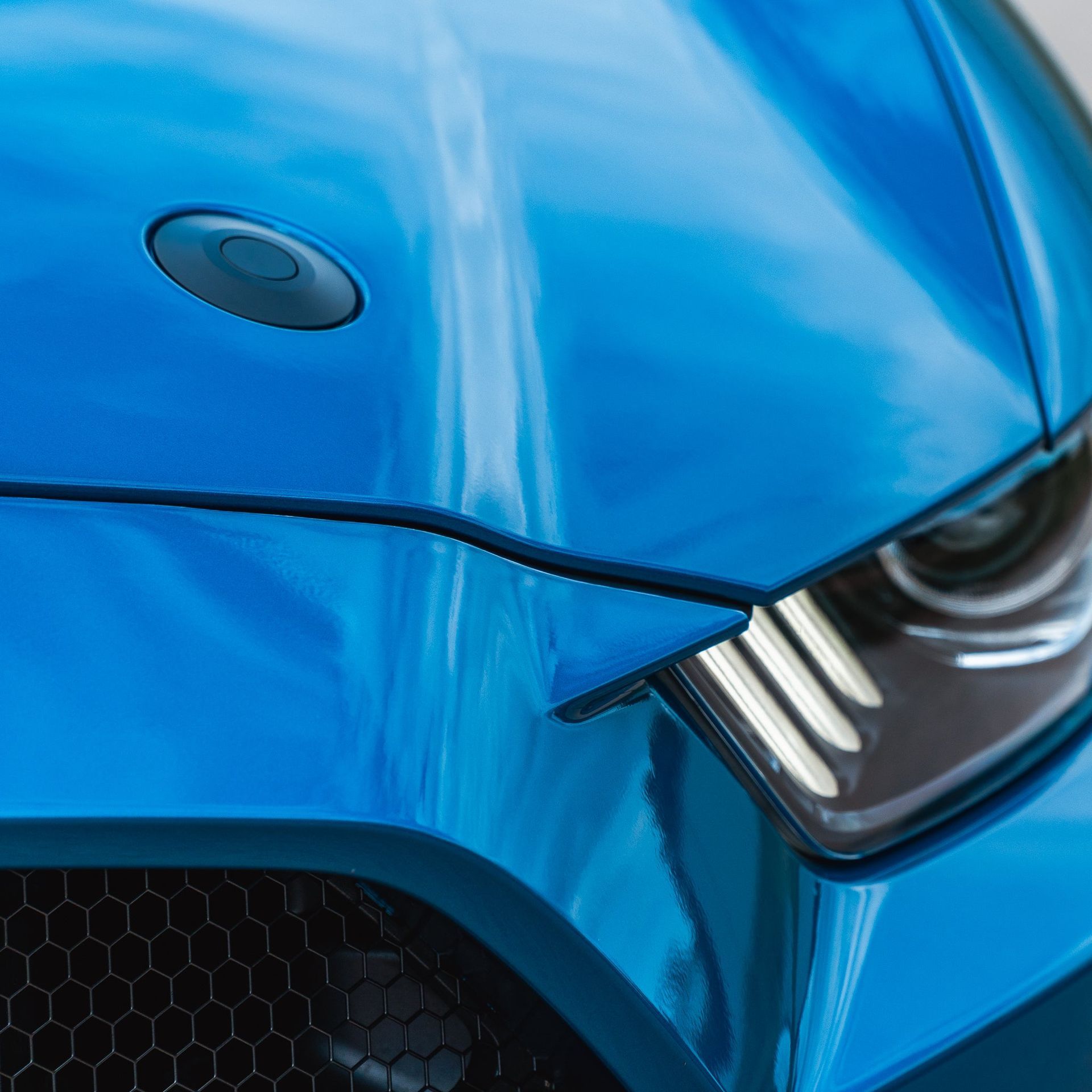 Close-up of a bright blue sports car front with a sleek headlight and black grille