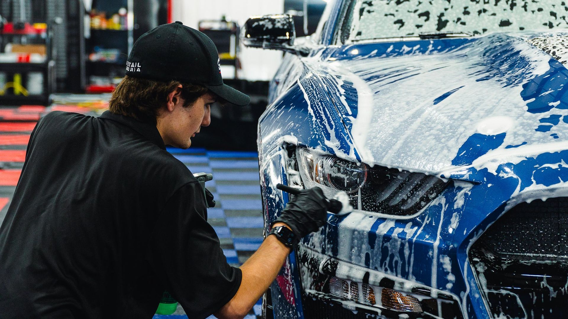 Person washing a blue sports car with soap in a garage workshop