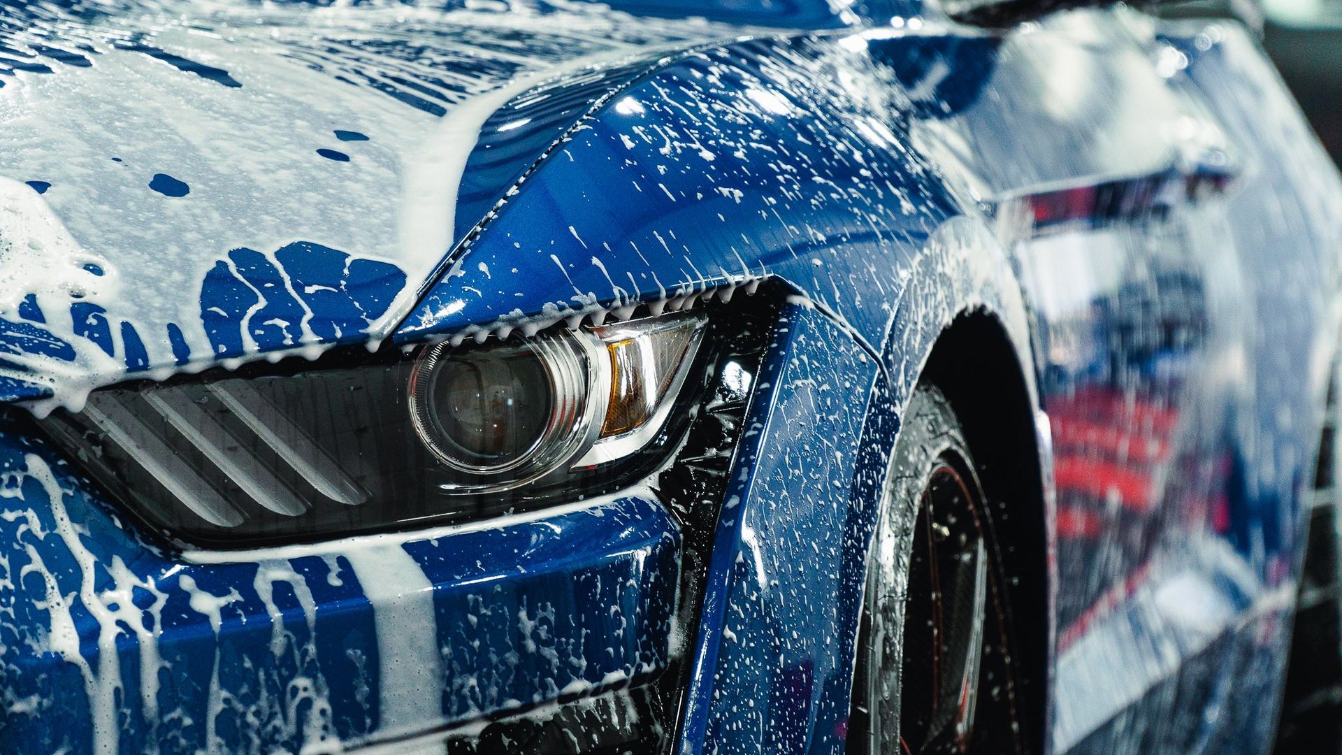 Blue sports car splashing through water during a wash, front headlight visible