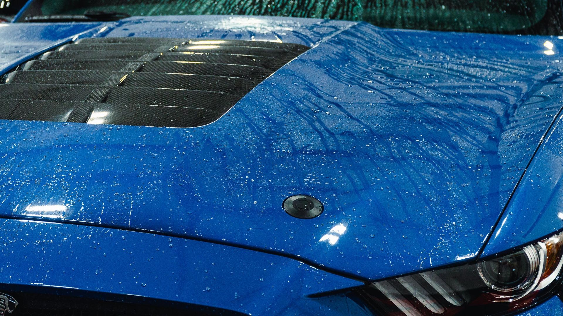 Blue sports car hood with raindrops and a black hood scoop, close-up detail