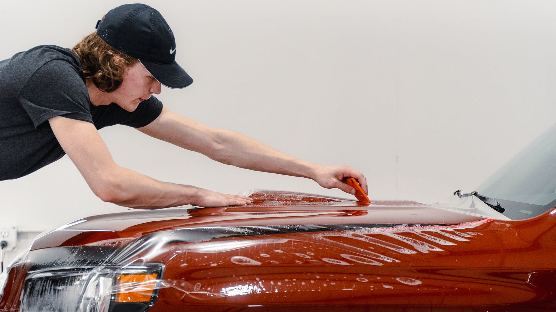 Person polishing a red car hood with a cloth in a garage
