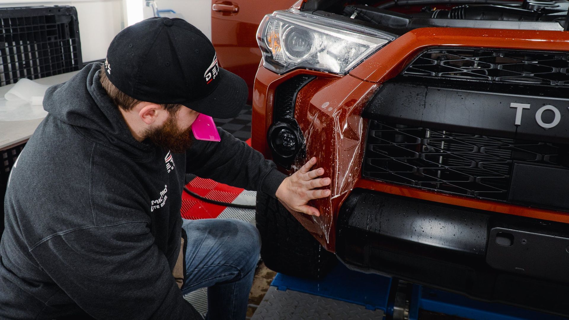 Mechanic inspecting a red Toyota truck’s front bumper in a garage